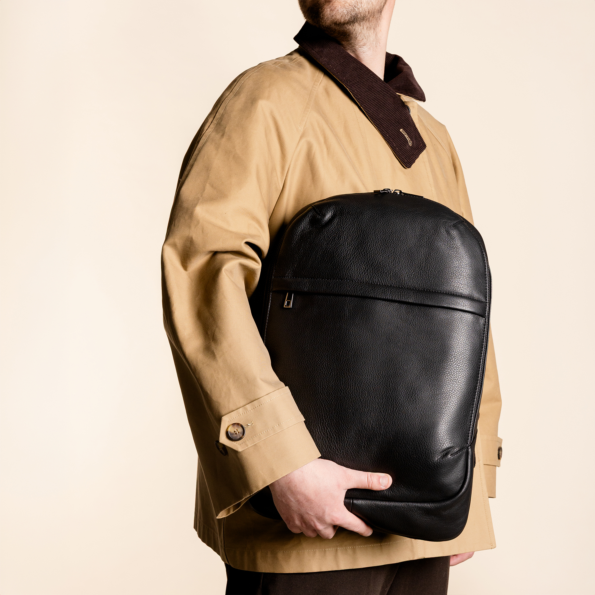 Man in a tan coat holding a black leather bag.