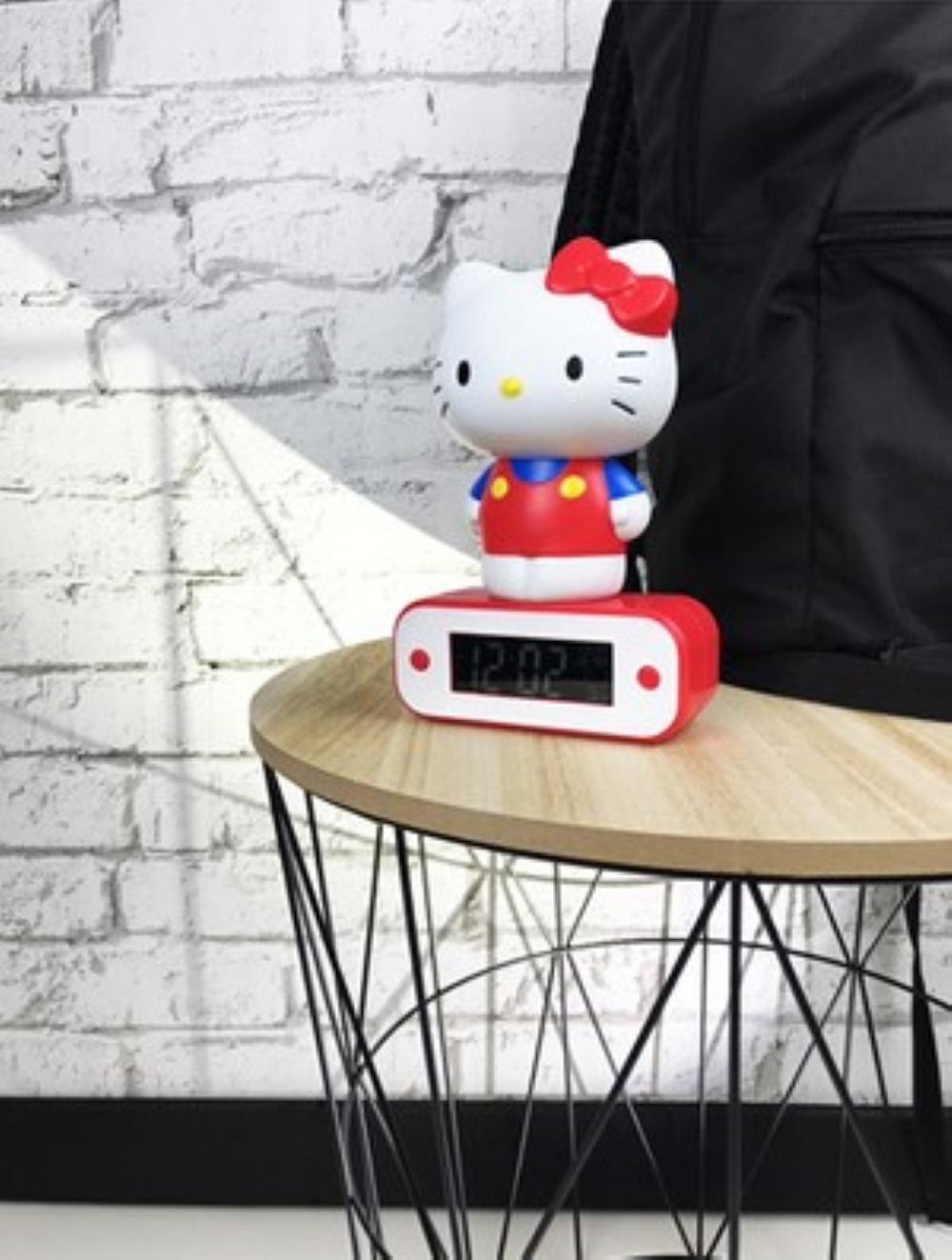 Budzik Hello Kitty na drewnianym stole na tle ceglanej ściany.