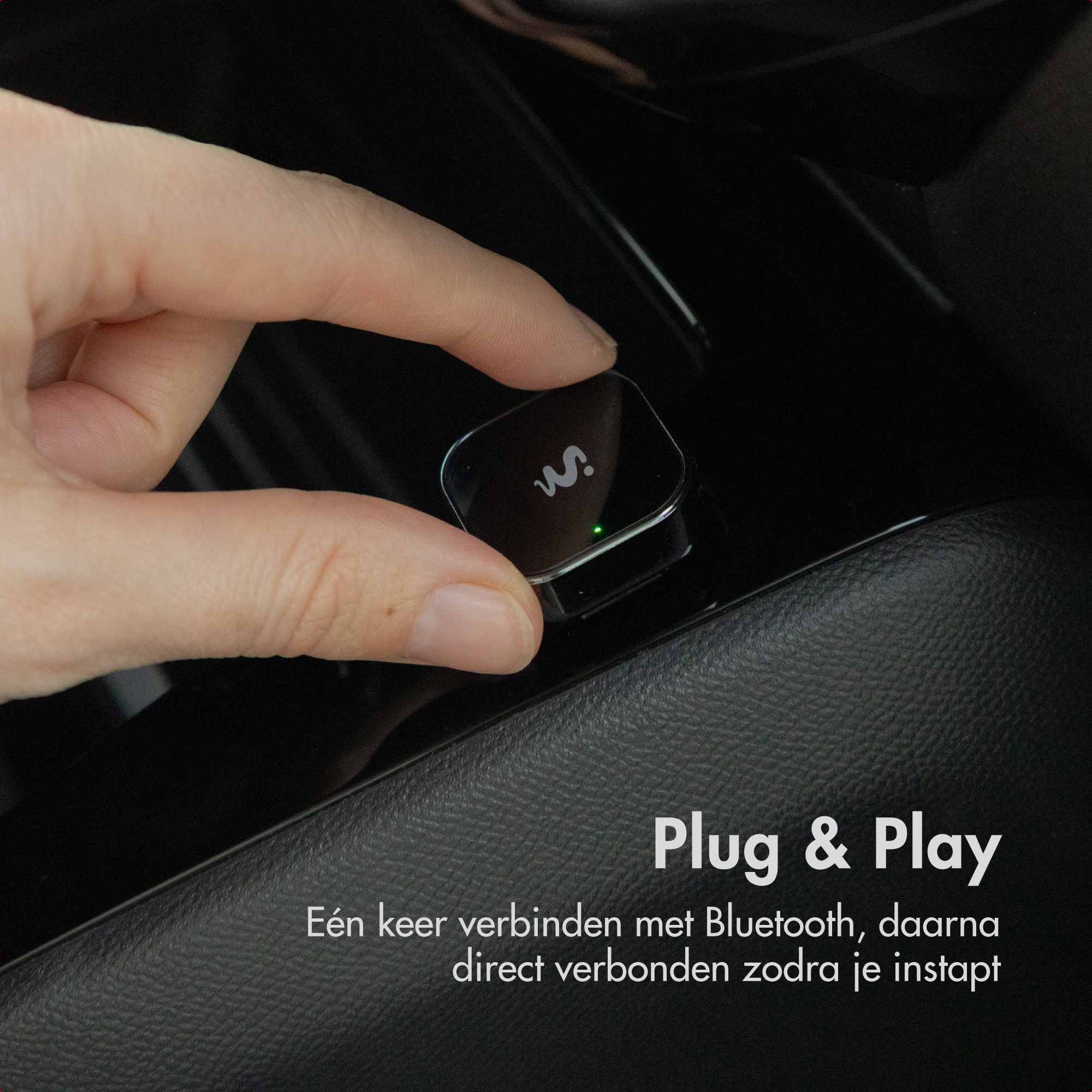 A hand holds a small black Bluetooth adapter with a green light.