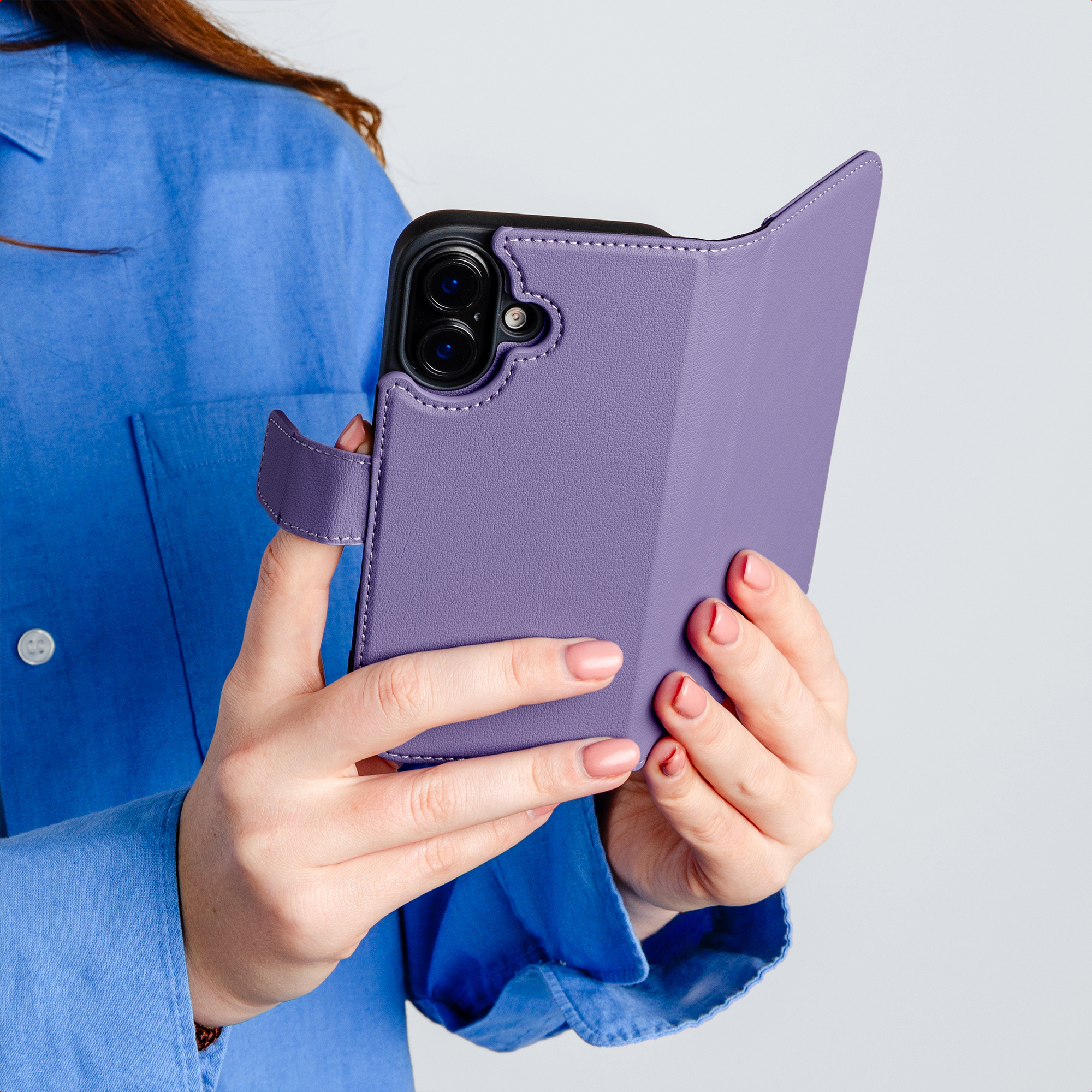 Person im blauen Hemd hält lila Handyhülle mit Handy darin.