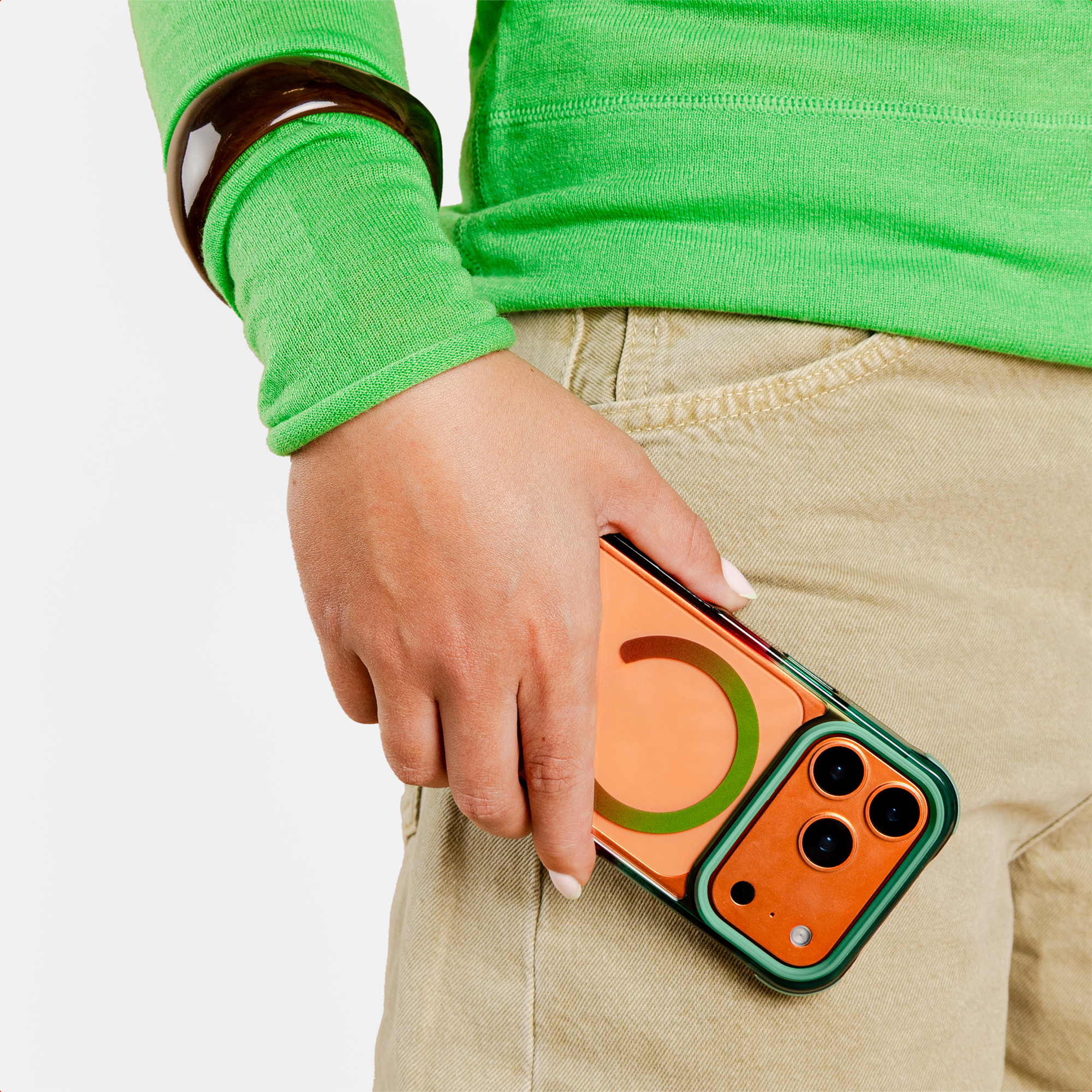 Persoon in cargo broek, groen topje, bruine armband houdt telefoon vast.