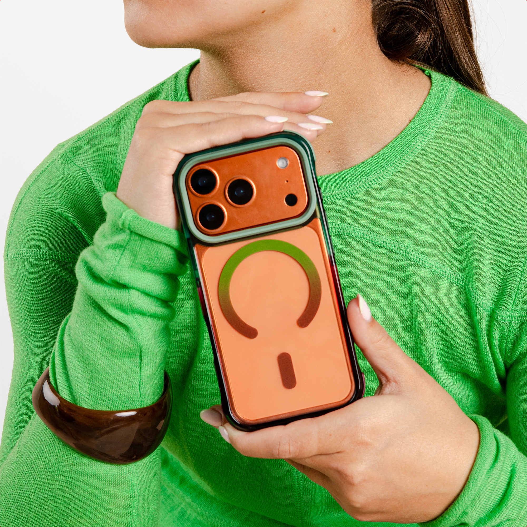 Een vrouw in een groene trui houdt een oranje iPhone hoesje met drie cameralenzen vast.