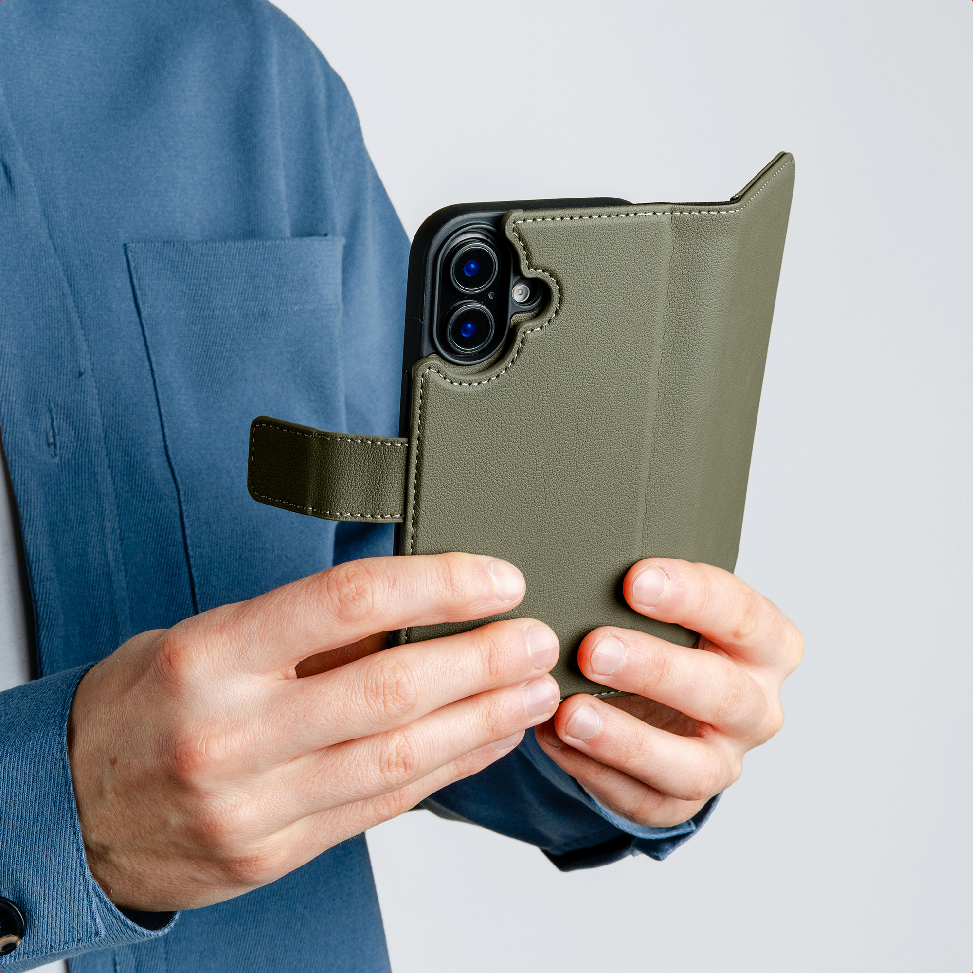 Person mit blauem Hemd hält ein grünes iPhone-Etui mit Kameras auf grauem Hintergrund.