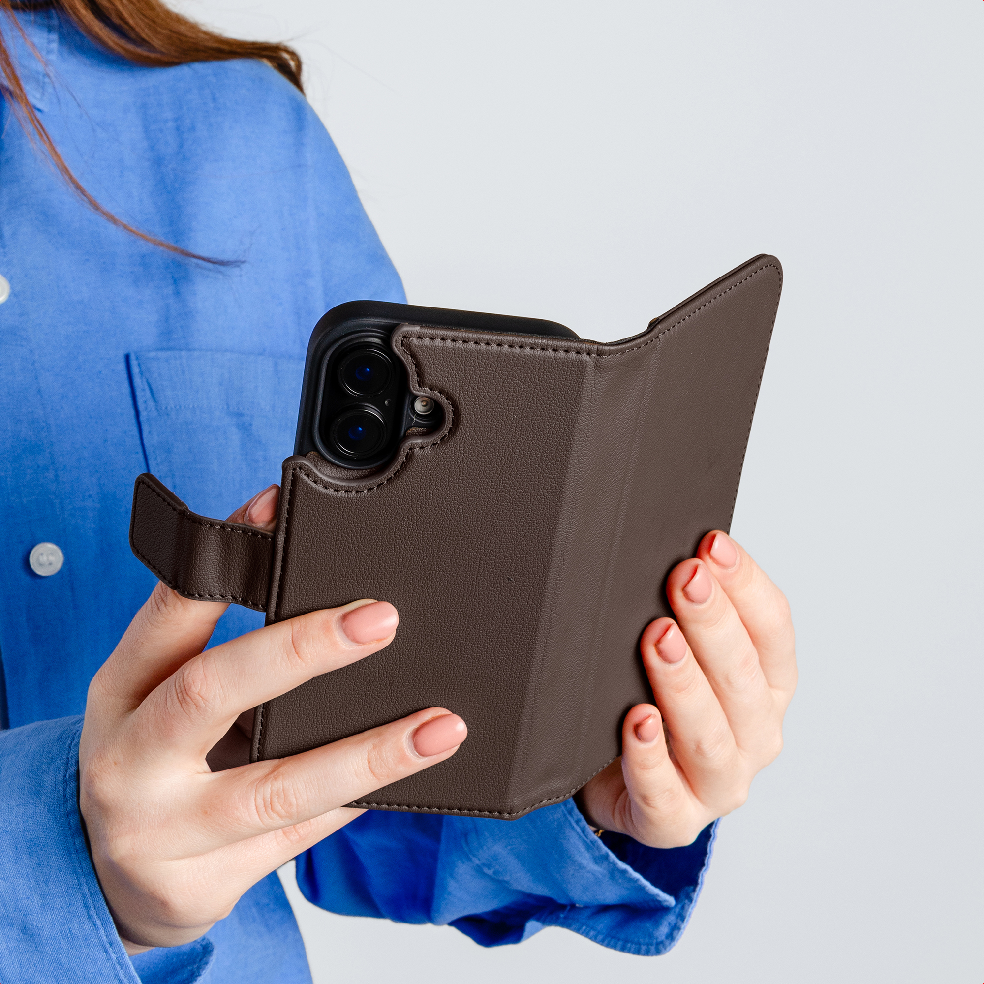 Eine Person in einem blauen Hemd hält eine braune Lederhülle mit einem Telefon darin.