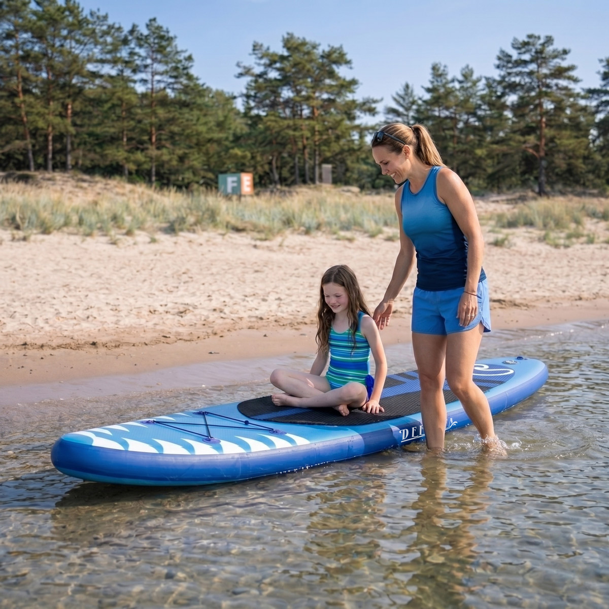 Frau und Mädchen auf einem Stand-Up-Paddle-Board am Strand, im flachen Wasser.