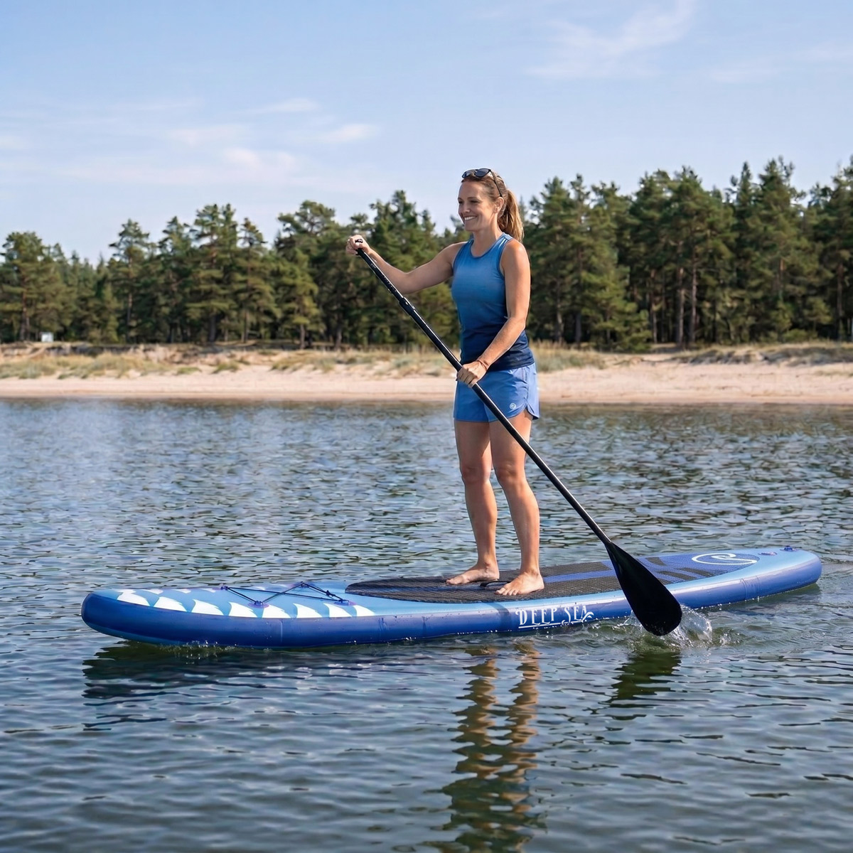Frau beim Paddleboarden auf blauem Wasser mit Bäumen und Strand im Hintergrund.