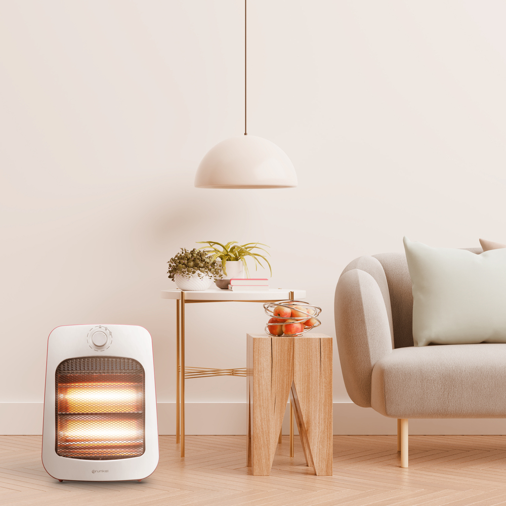 Un calentador eléctrico blanco y rojo brilla con luz naranja en una habitación con sofá.