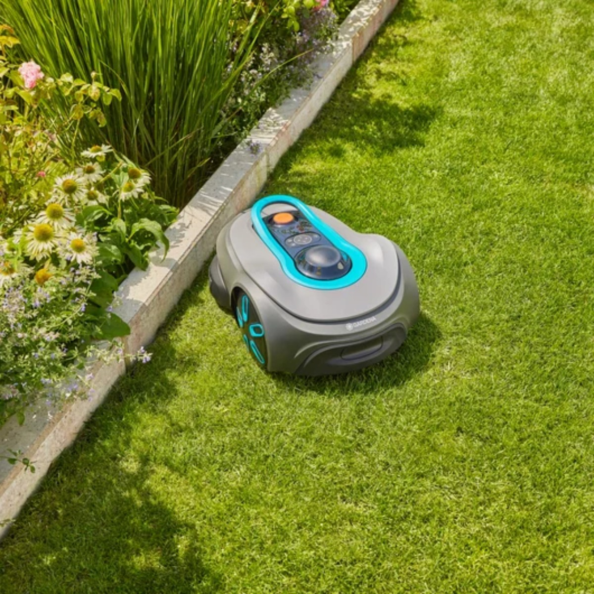 Un robot cortacésped gris con detalles azules está sobre un césped verde junto a flores.