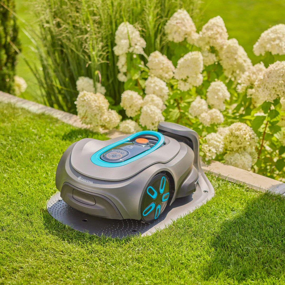 Un tosaerba robotizzato grigio con accenti blu si trova su una base di ricarica in un prato verde.