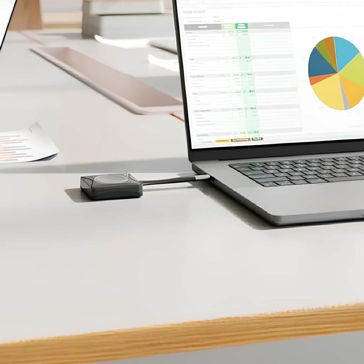 Un adattatore grigio si collega a un laptop che mostra un grafico a torta e un foglio di calcolo.
