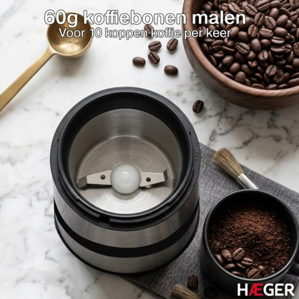 Kaffeemühle mit Mahlgut, Kaffeebohnen, Löffel und Pinsel auf Marmortisch.