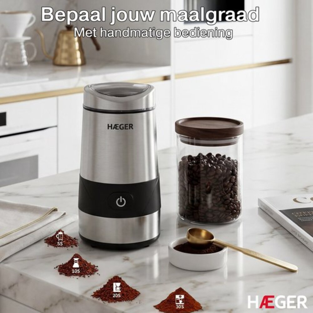 Edelstahl-Kaffeemühle mit Kaffeebohnenglas, Pulver und Löffel auf Marmor.