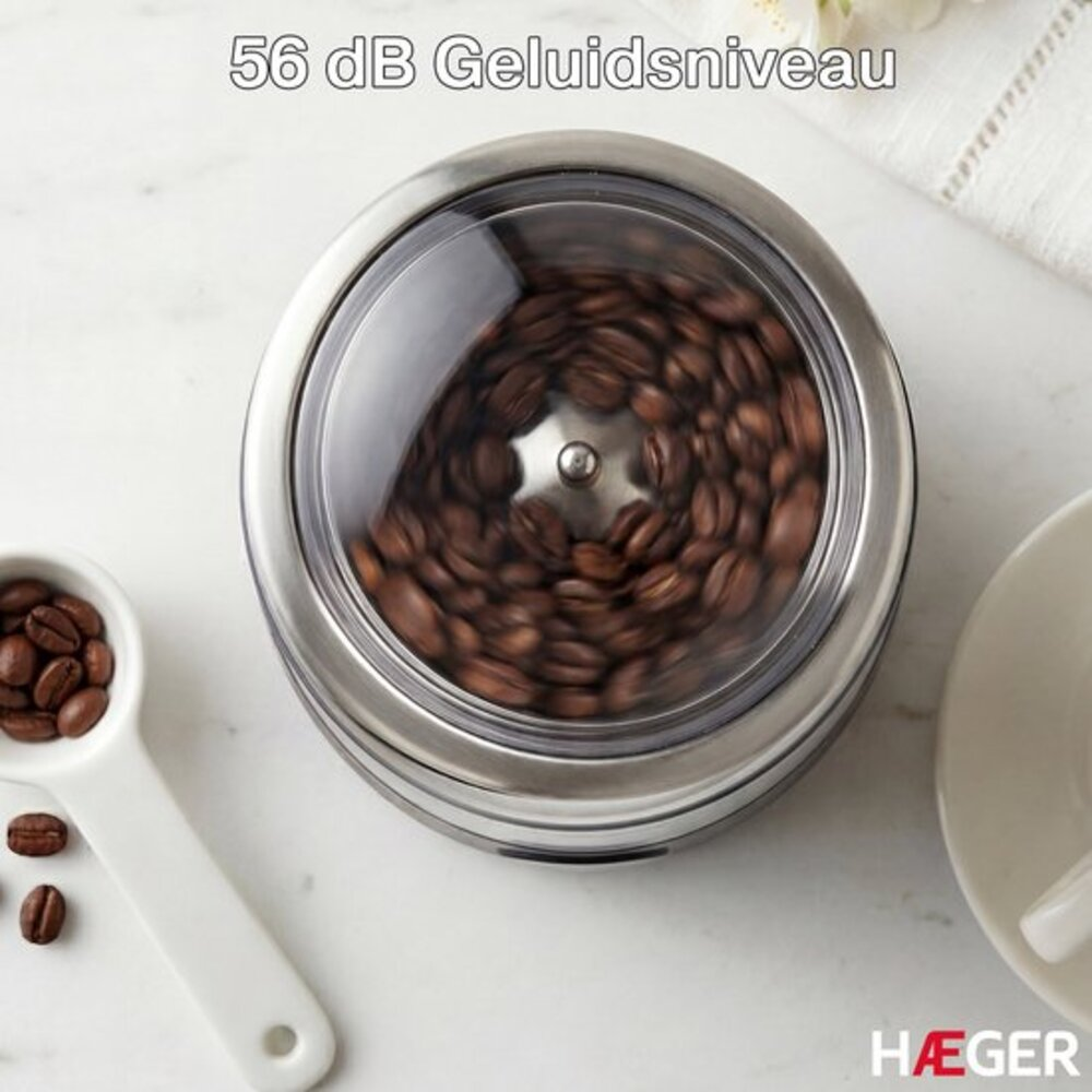 Kaffeebohnen mahlen in einem elektrischen Mahlwerk, mit einer Kaffeelöffel daneben.