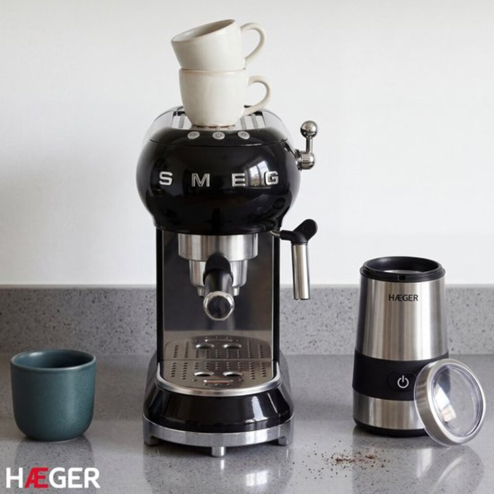 Schwarze Smeg Espressomaschine mit zwei Tassen darauf, daneben eine Mühle.
