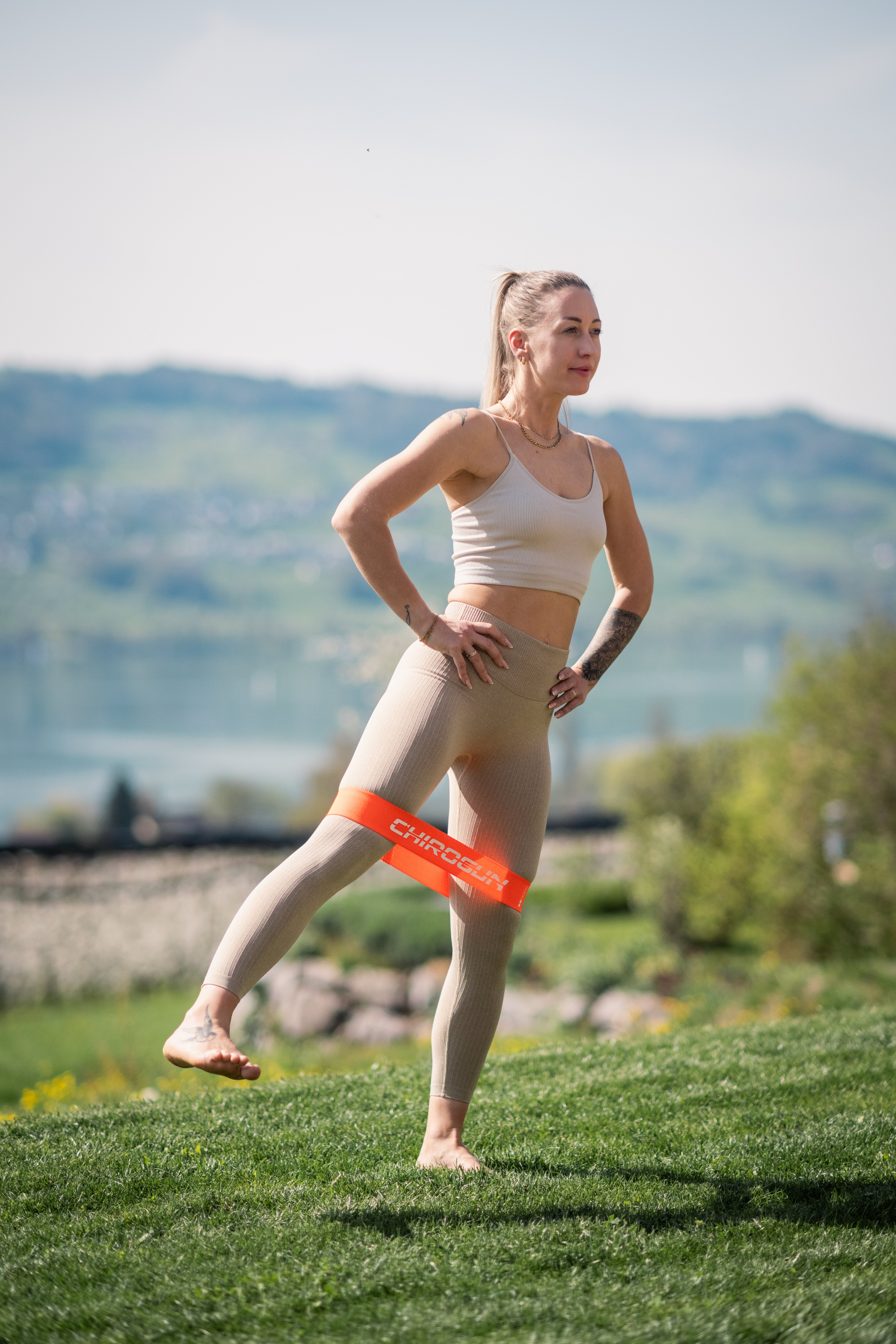 Frau trainiert mit orangefarbenem Widerstandsband im Freien, mit Blick auf Hügel.