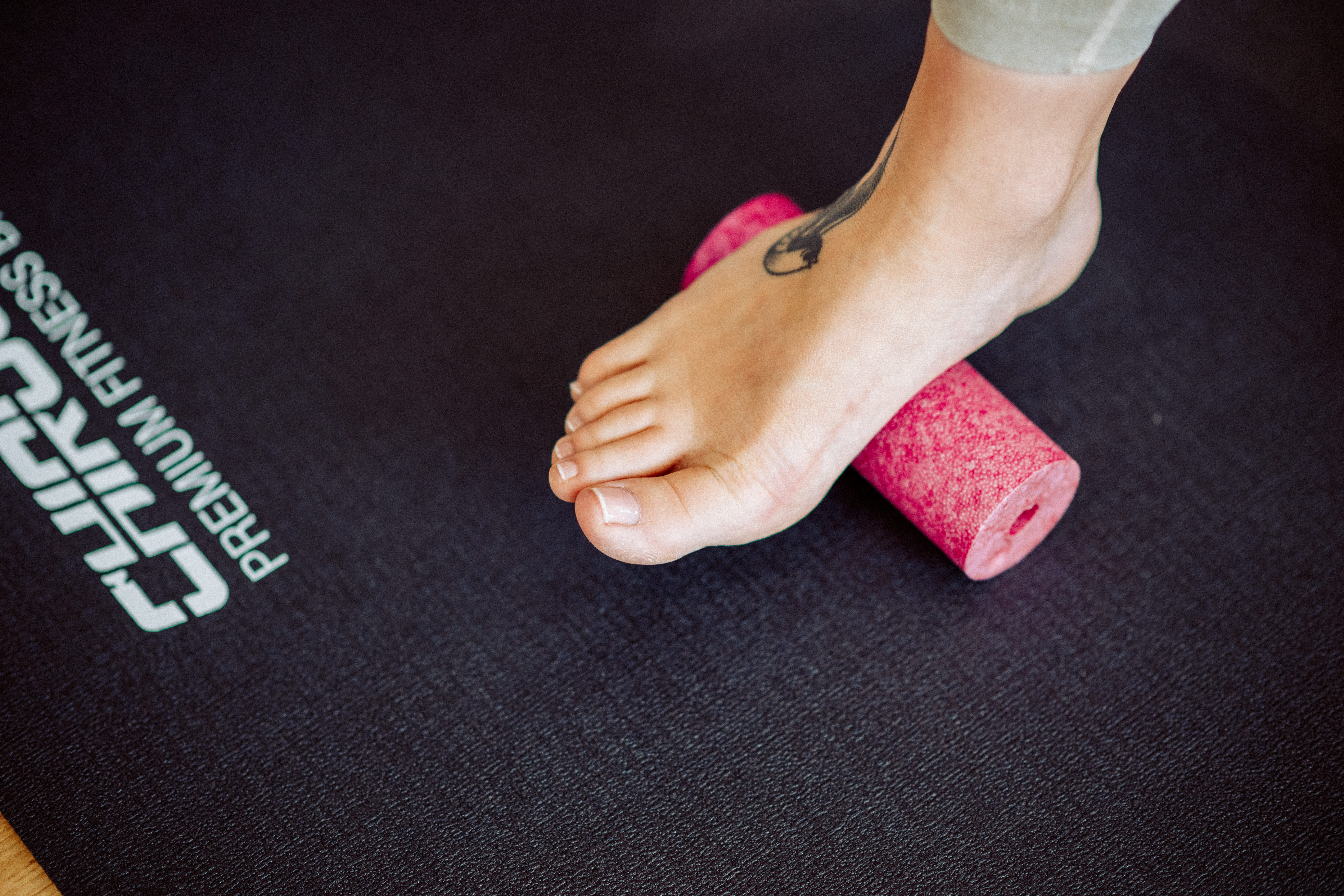 Ein Fuß mit Tattoo rollt über eine rosa Schaumstoffrolle auf einer schwarzen Matte.