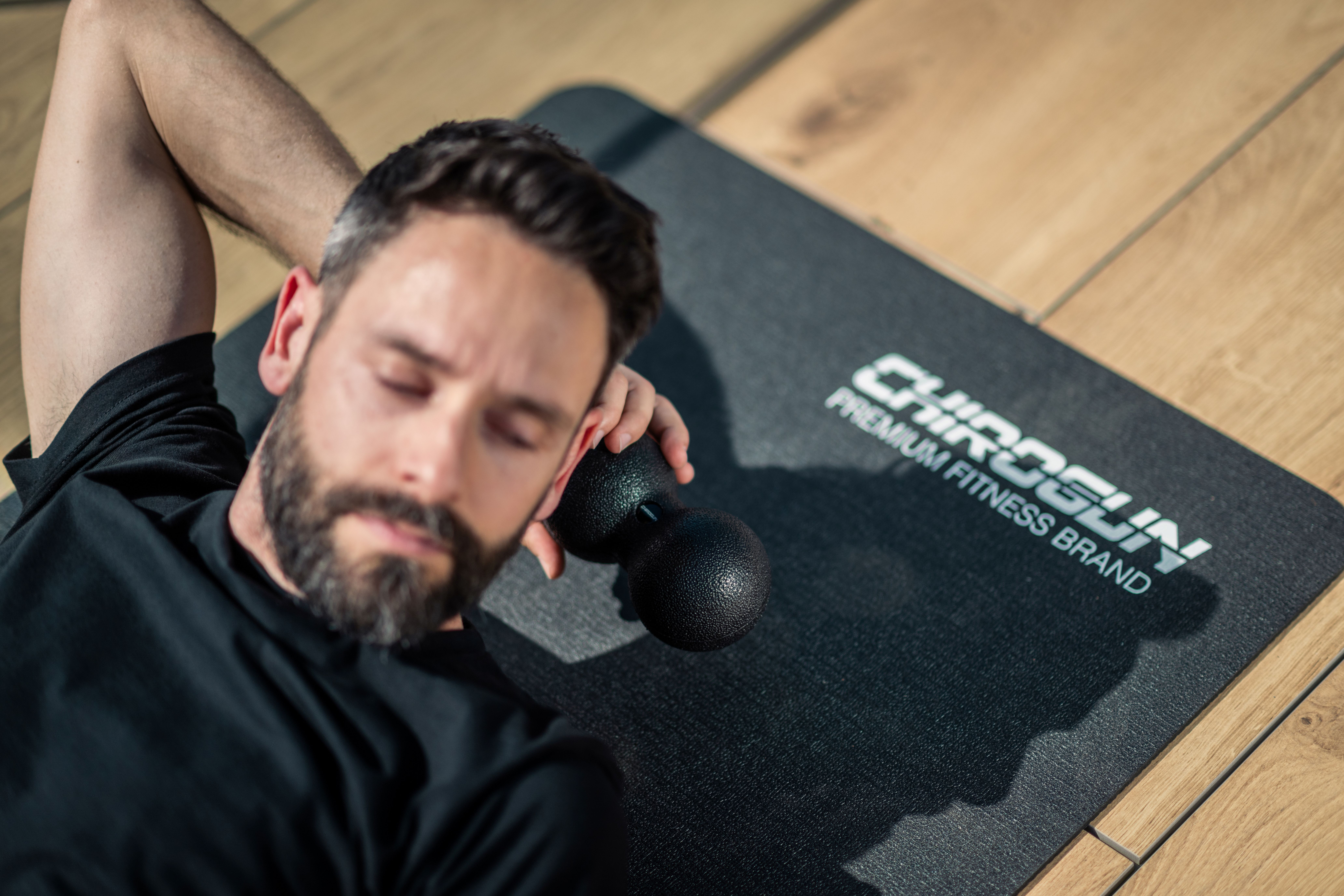 Mann liegt auf Matte mit Massageball im Nacken.