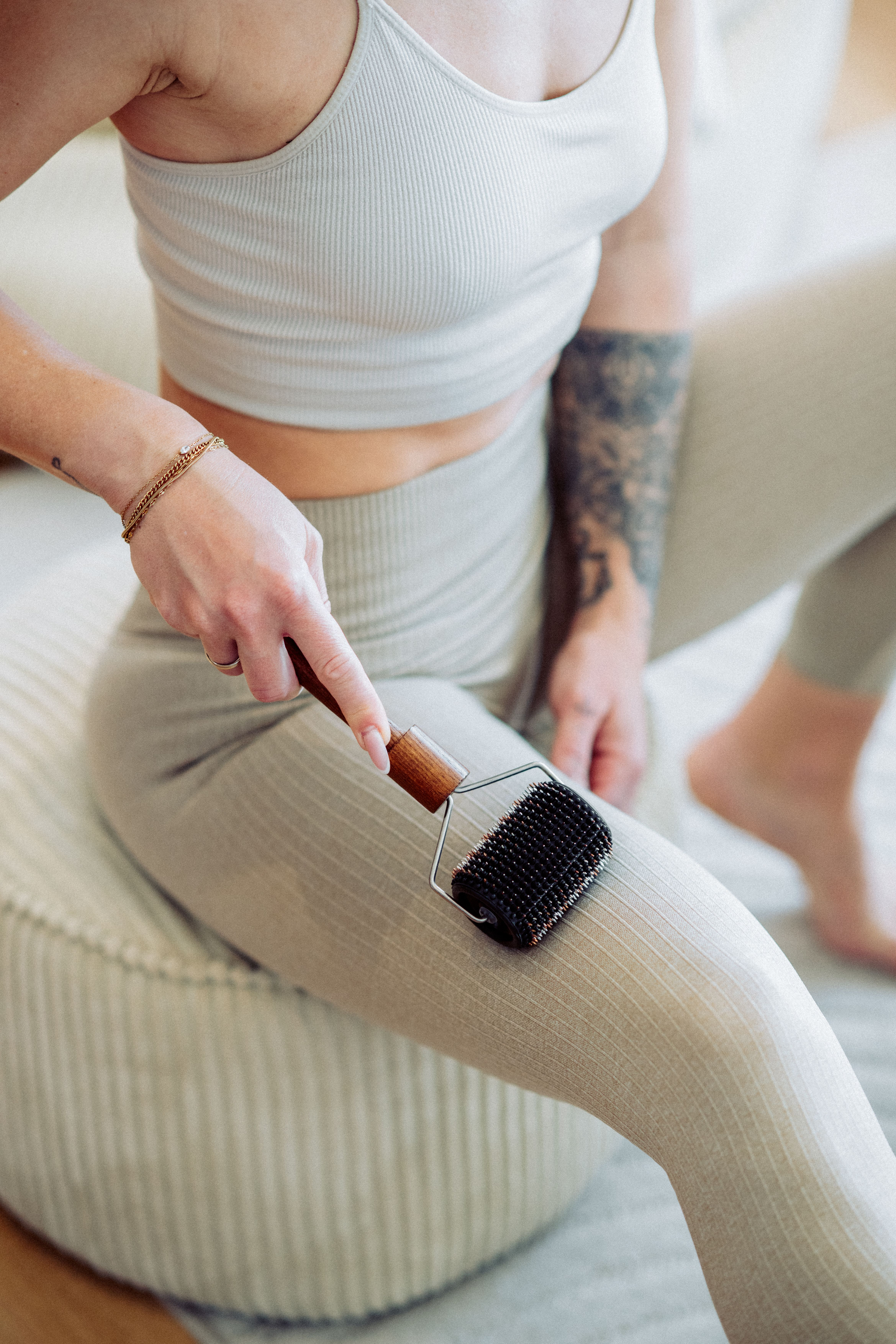 Eine Frau mit Tattoo rollt ihre Beinmuskulatur mit einem Massagegerät.