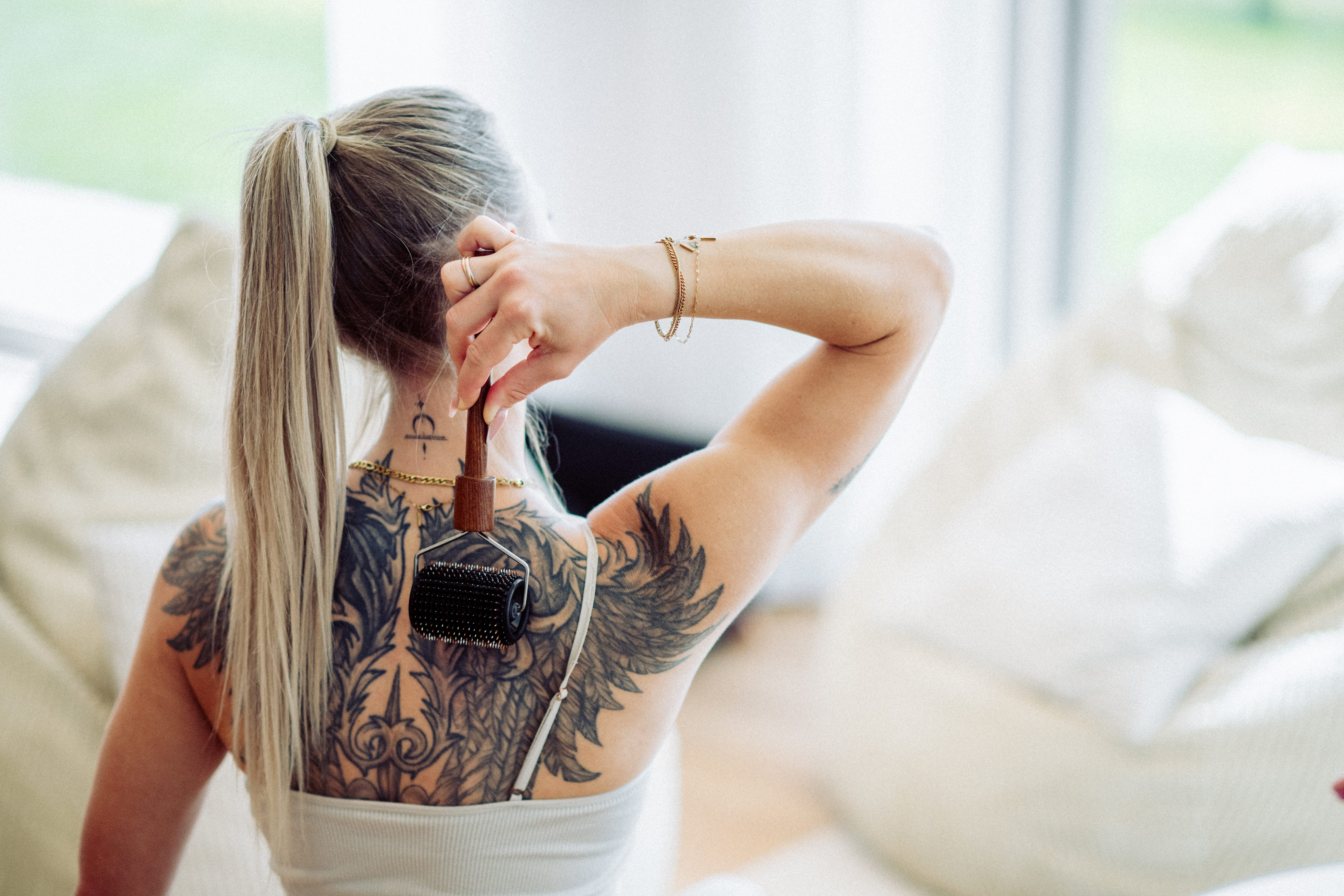 Frau mit Tattoo am Rücken benutzt eine Massagebürste.