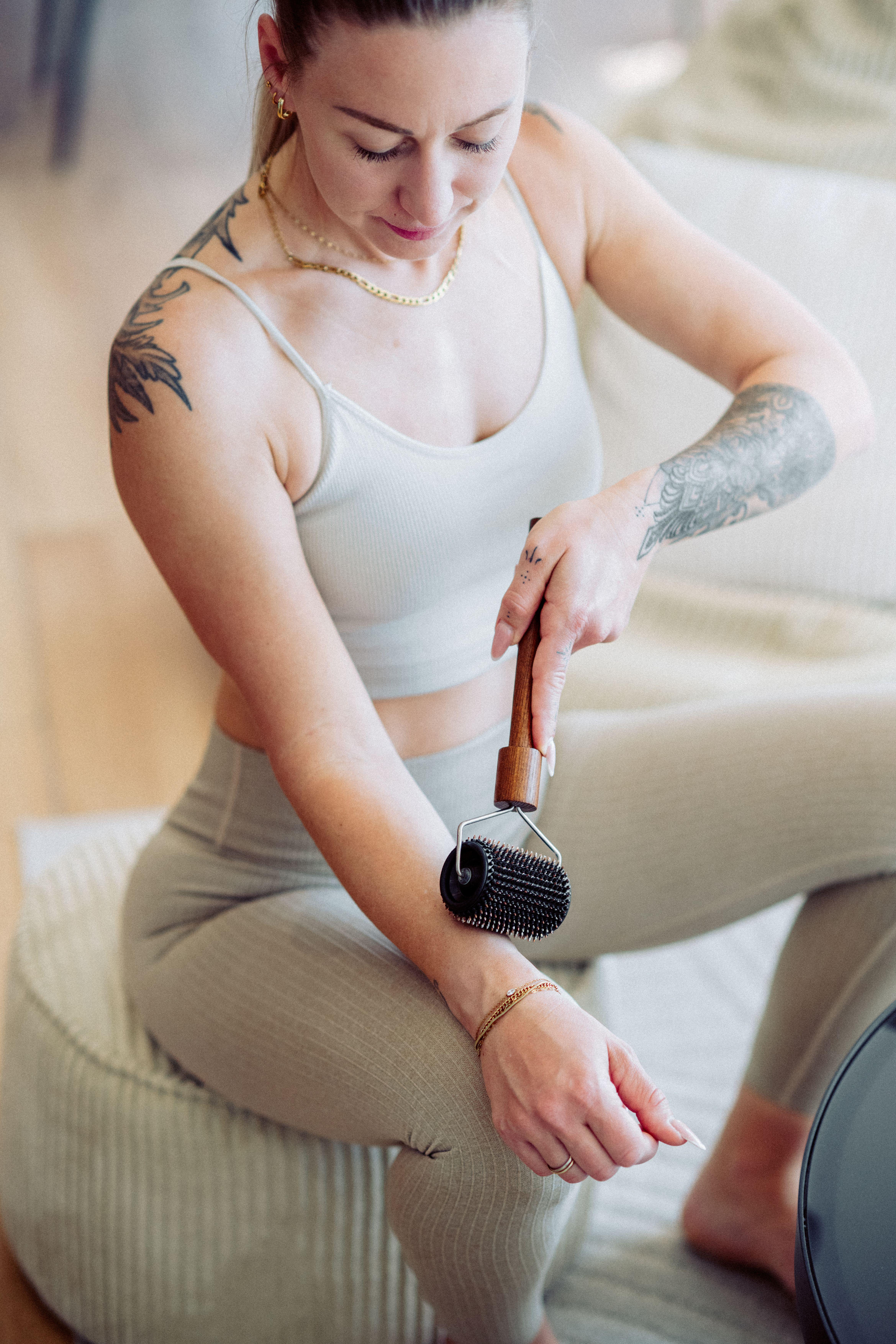 Frau mit Tattoos rollt sich mit einem Massagegerät den Arm.