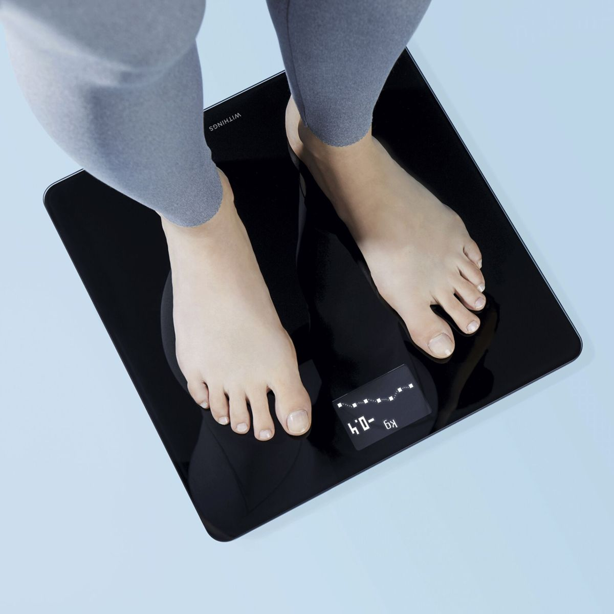 Stopy na czarnej wadze z cyfrowym wyświetlaczem pokazującym -0,4 kg.