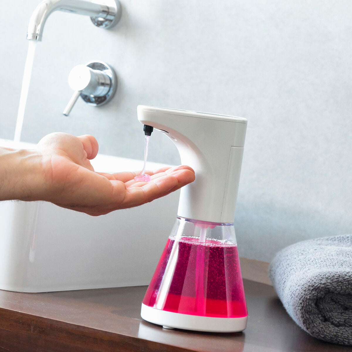 Ein Händedruck unter einem Seifenspender mit rosa Seife, ein Wasserhahn tropft.