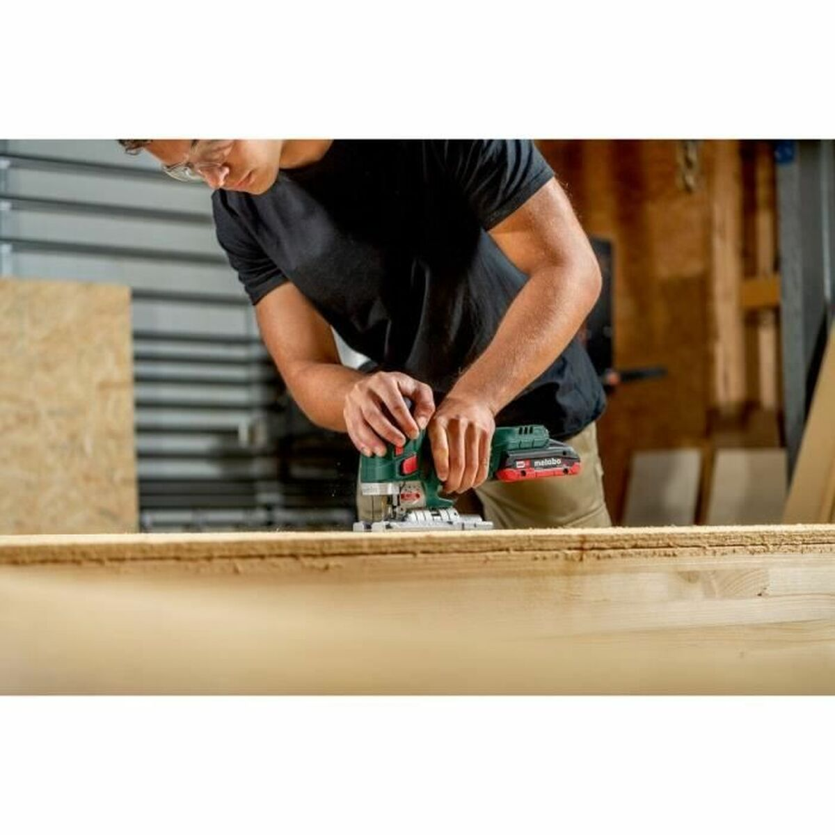 A man wearing safety glasses saws wood with a jigsaw.