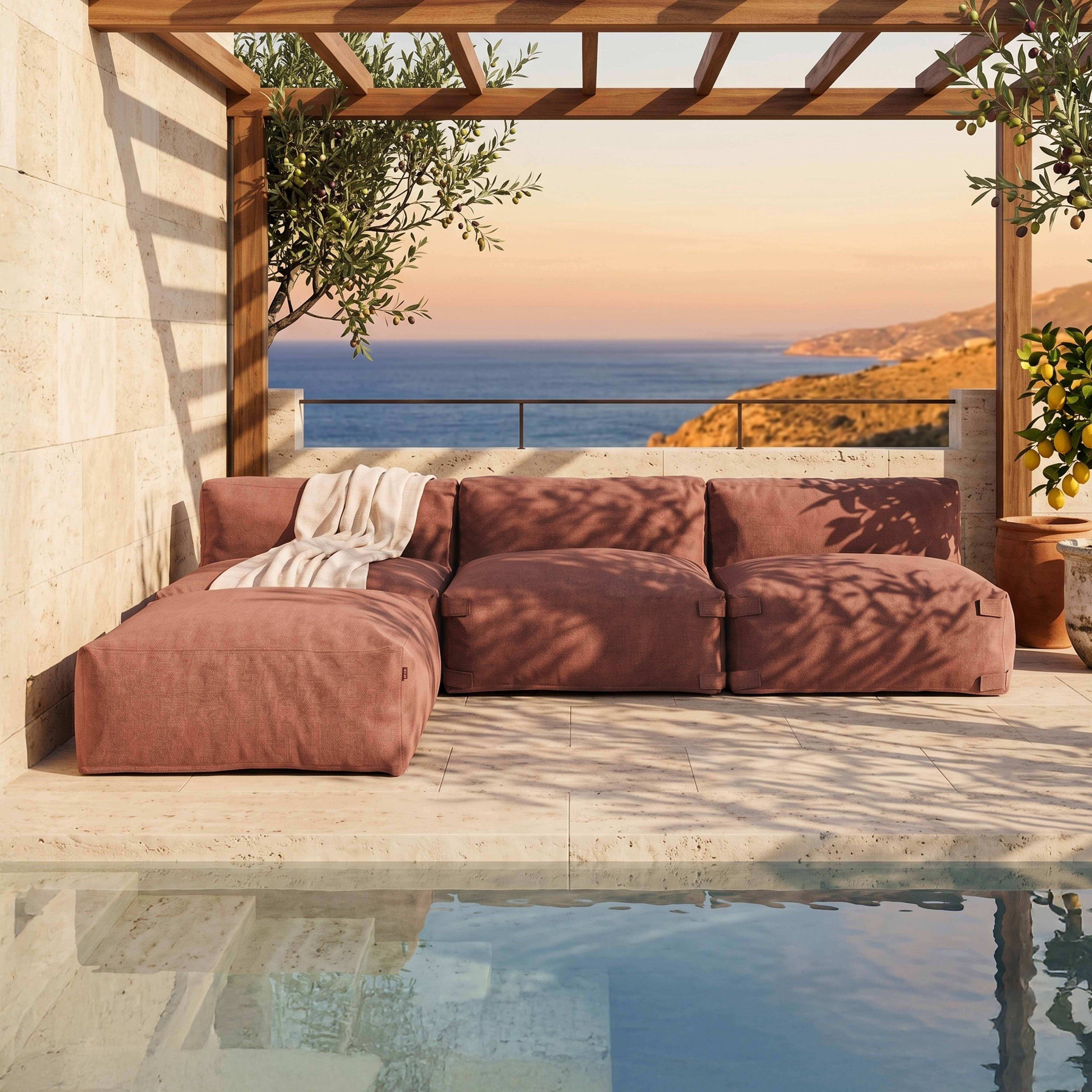 Ein rosafarbener Loungesofa steht auf einer Terrasse mit Blick auf das Meer.