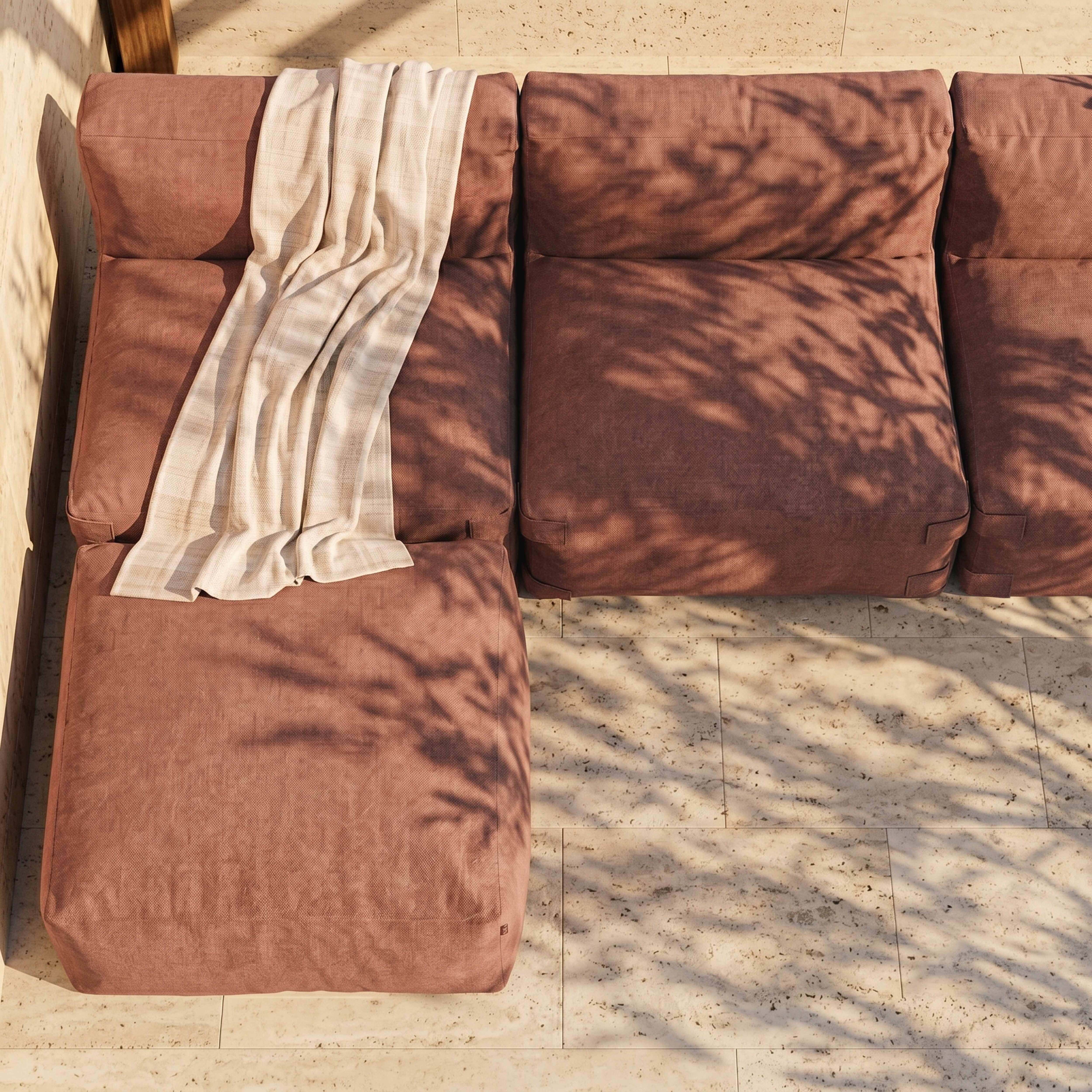 Ein rosafarbener Ecksofa mit einer beigen Decke, beschattet von Blättern.
