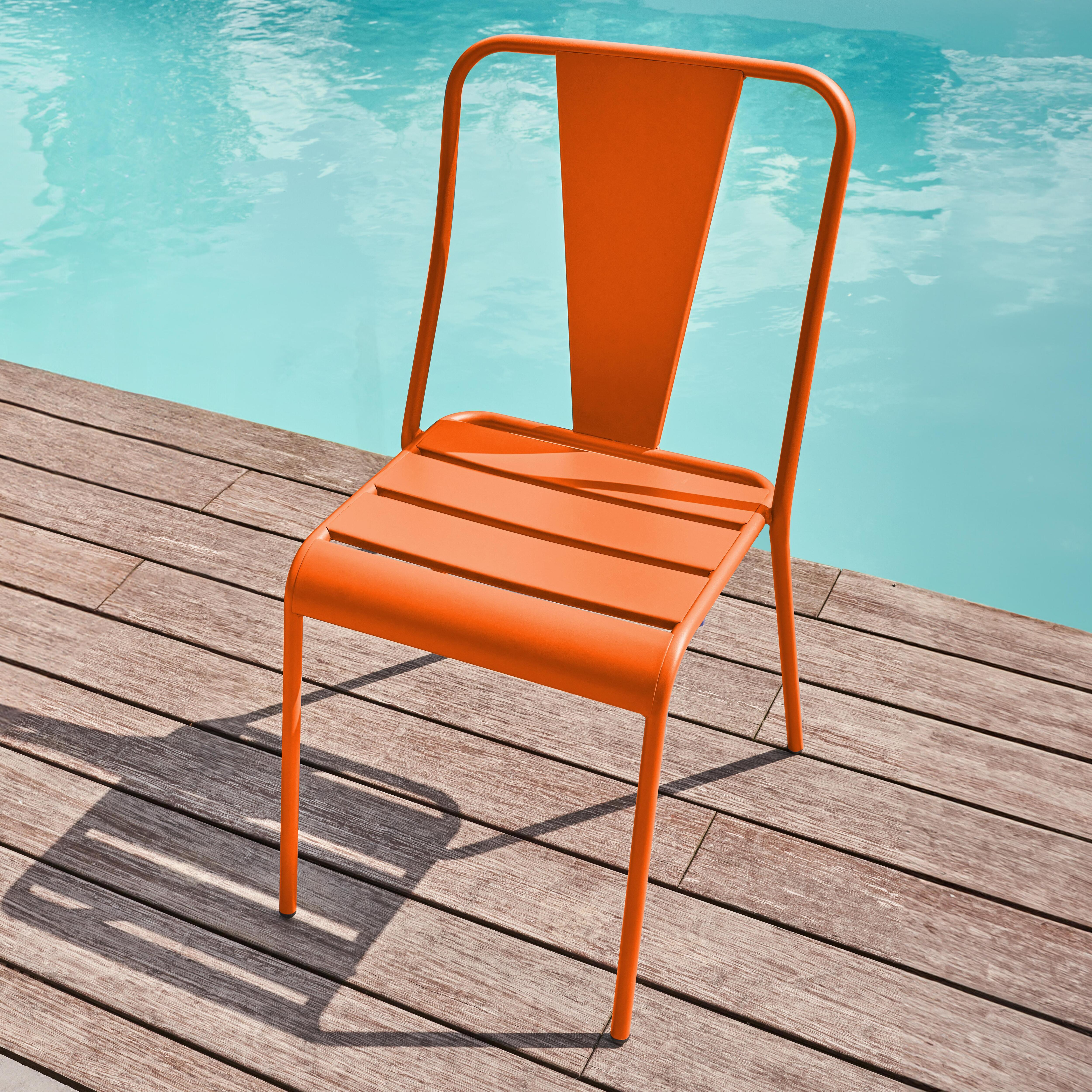 Eine orangefarbene Metallstuhl steht auf einer Holzterrasse neben einem Pool.