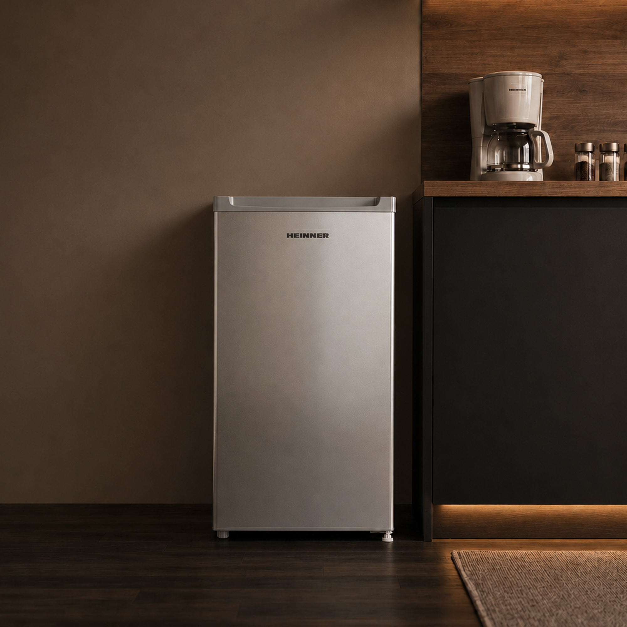 Un réfrigérateur argenté à côté d'une armoire noire avec une cafetière.