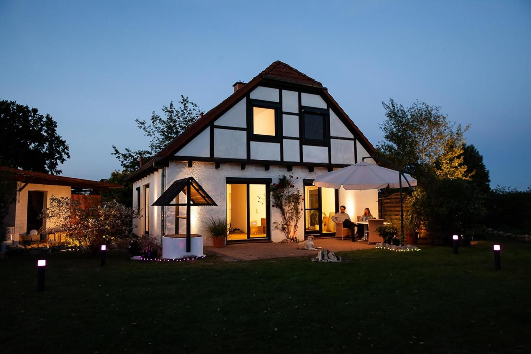 Ein Haus mit Fachwerk, ein Brunnen und zwei Hunde im Garten bei Dämmerung.