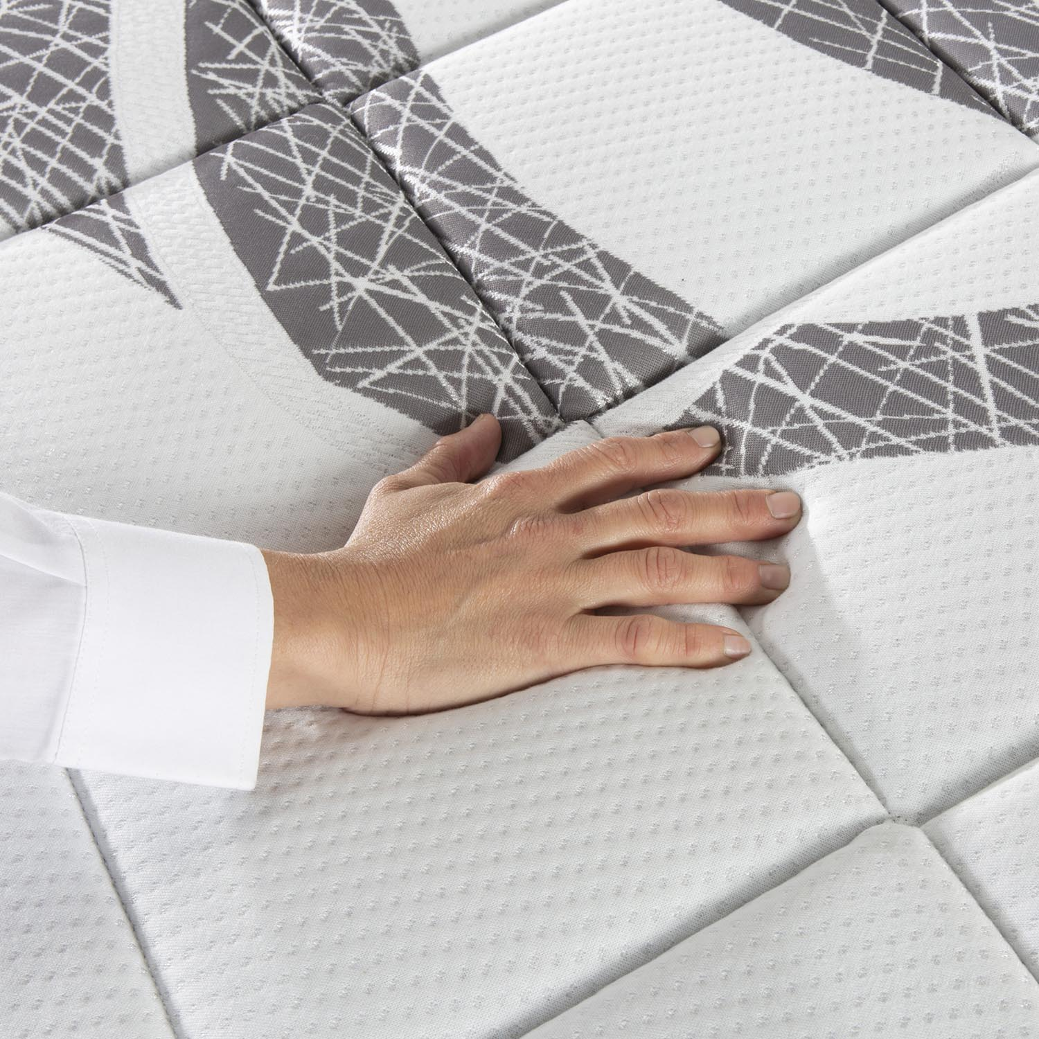 Una mano presiona un colchón blanco con patrón gris.