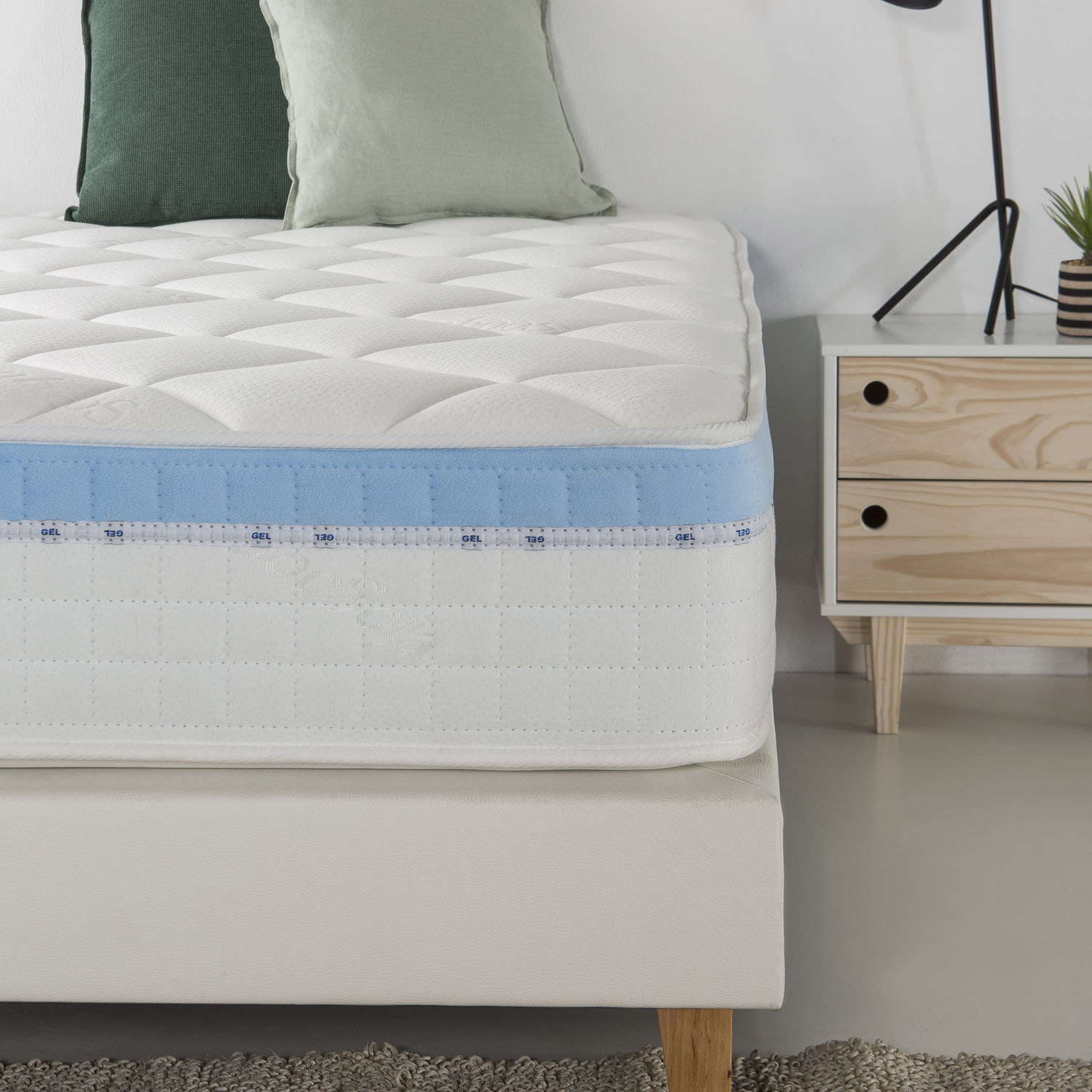 Un colchón blanco con raya azul, dos almohadas y una mesita de noche.