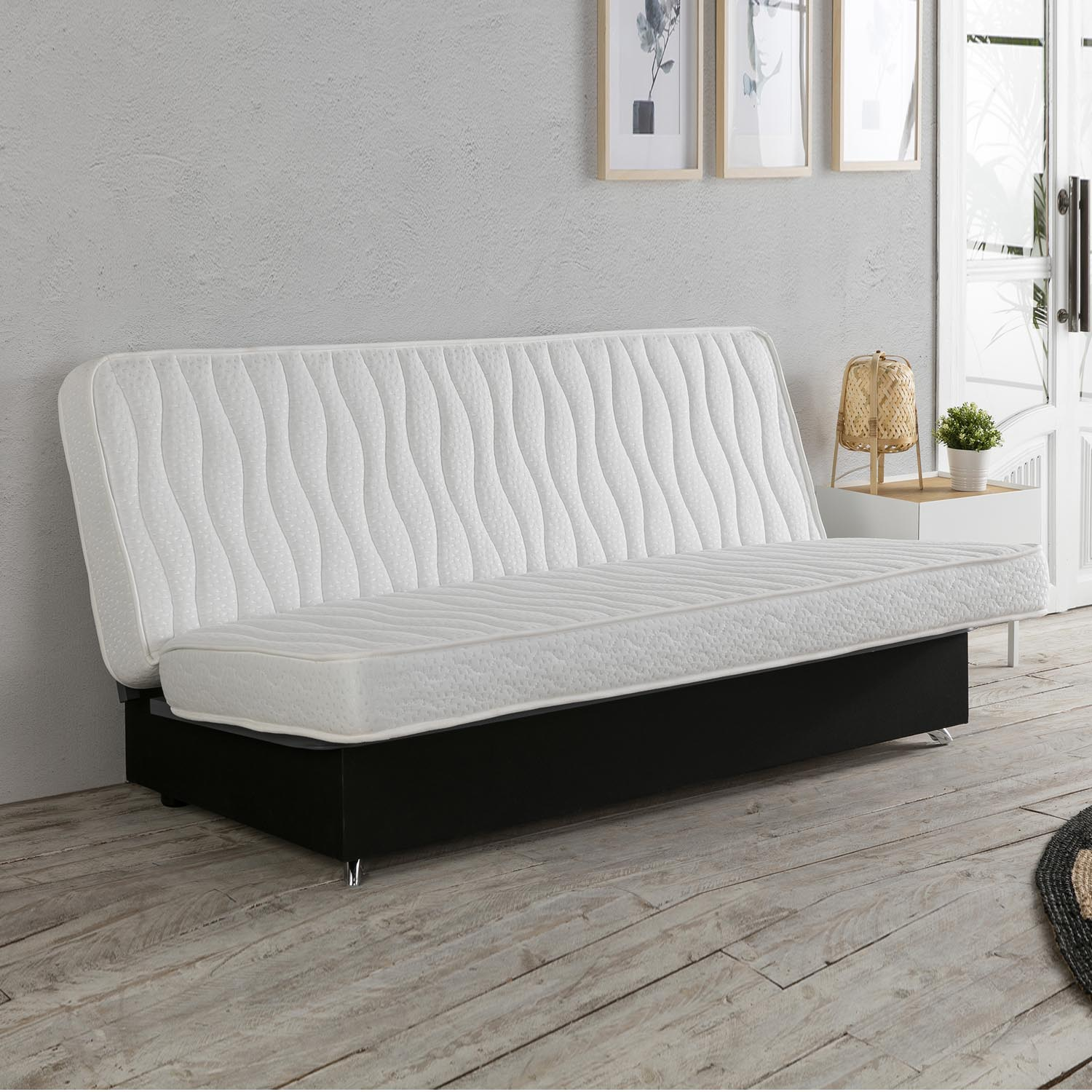 Un sofá cama con colchón blanco y base negra descansa sobre suelo de madera.