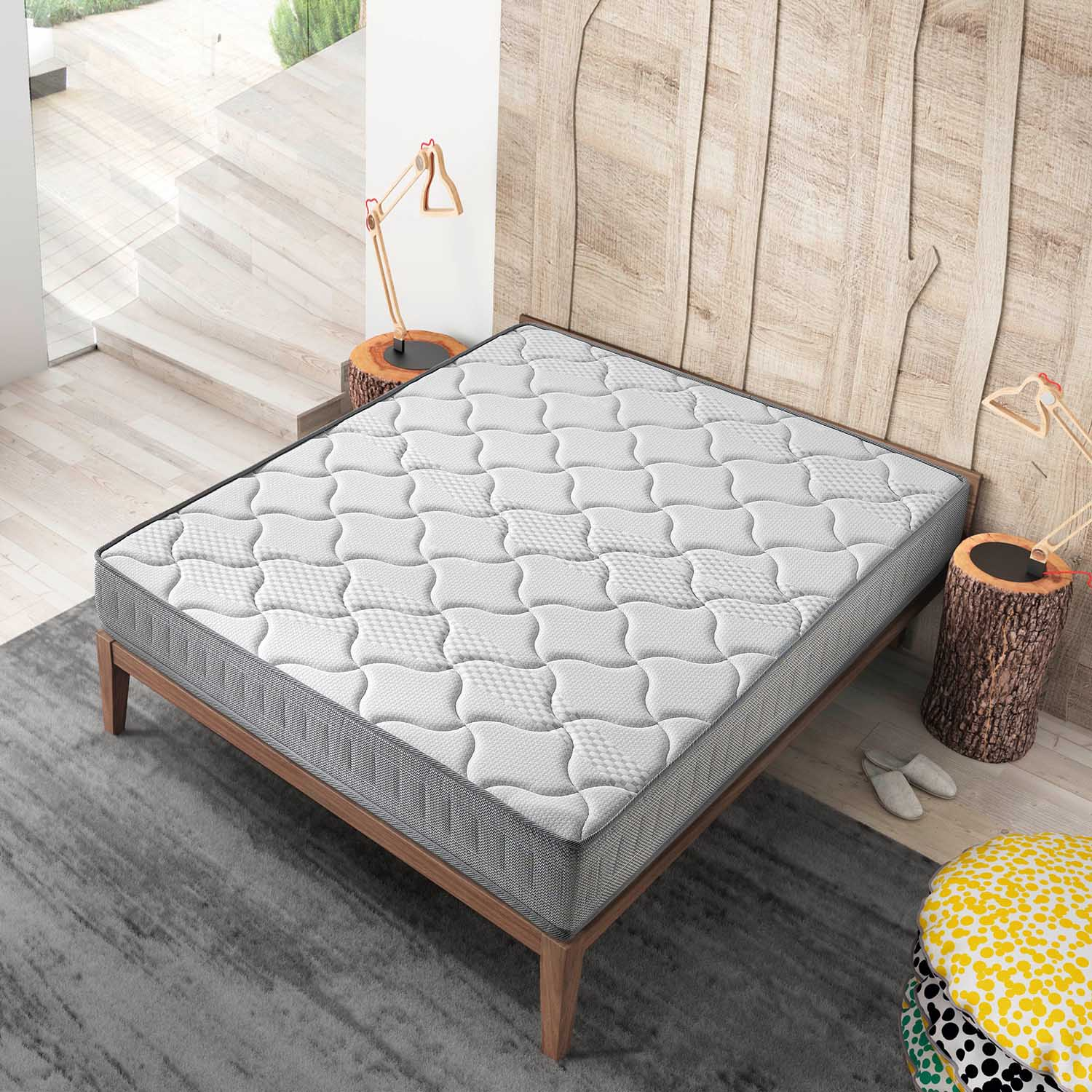 Un colchón blanco con borde gris sobre un marco de cama de madera en una alfombra gris.