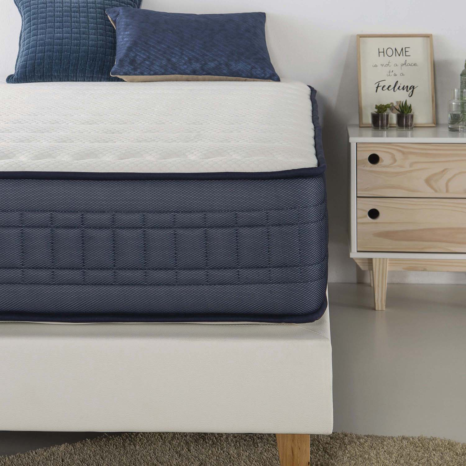 Una cama con colchón azul y almohadas blancas, junto a una mesita de noche con decoración.