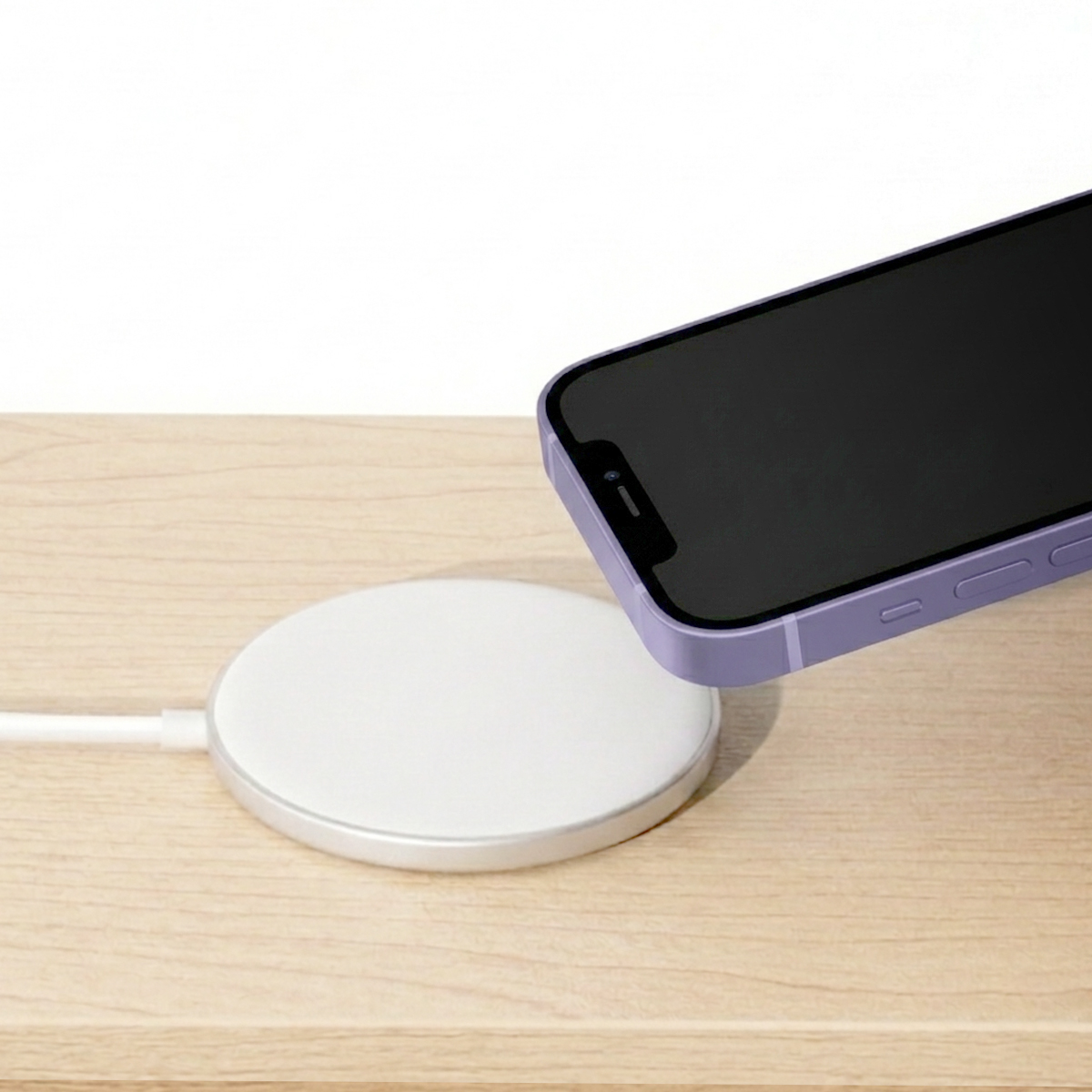 A purple phone is being placed over a white charging pad connected to a cable.