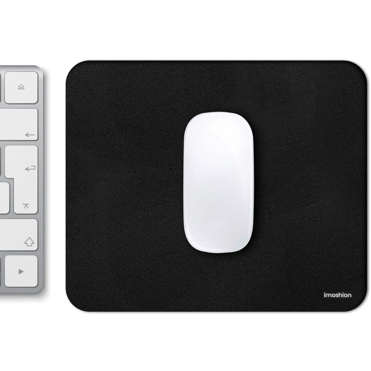 A white wireless mouse rests on a black mousepad next to a silver keyboard.