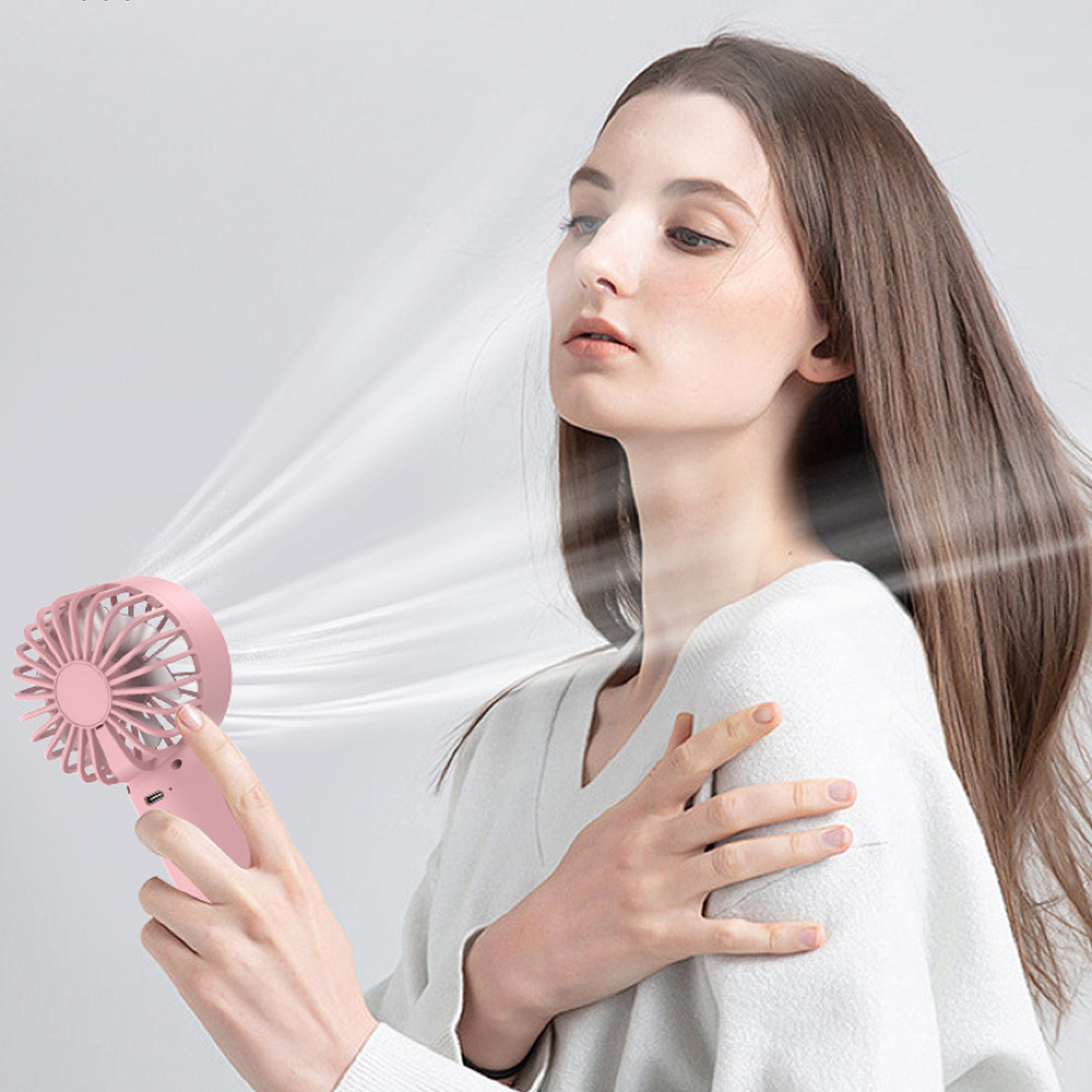 Eine Frau hält einen rosa Ventilator, der kühle Luft auf ihr Gesicht bläst.