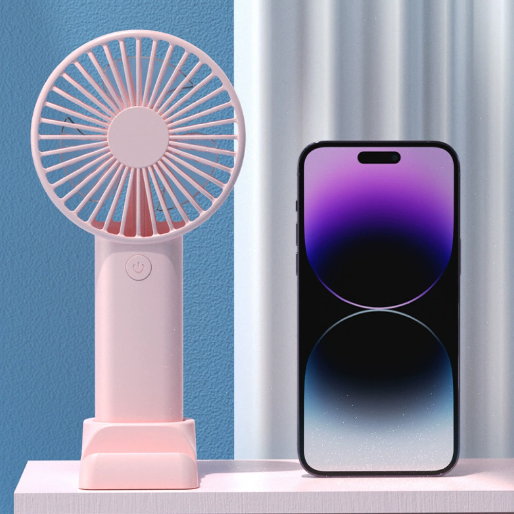 Ein rosa Ventilator und ein Smartphone mit lila Hintergrund auf einem Tisch.