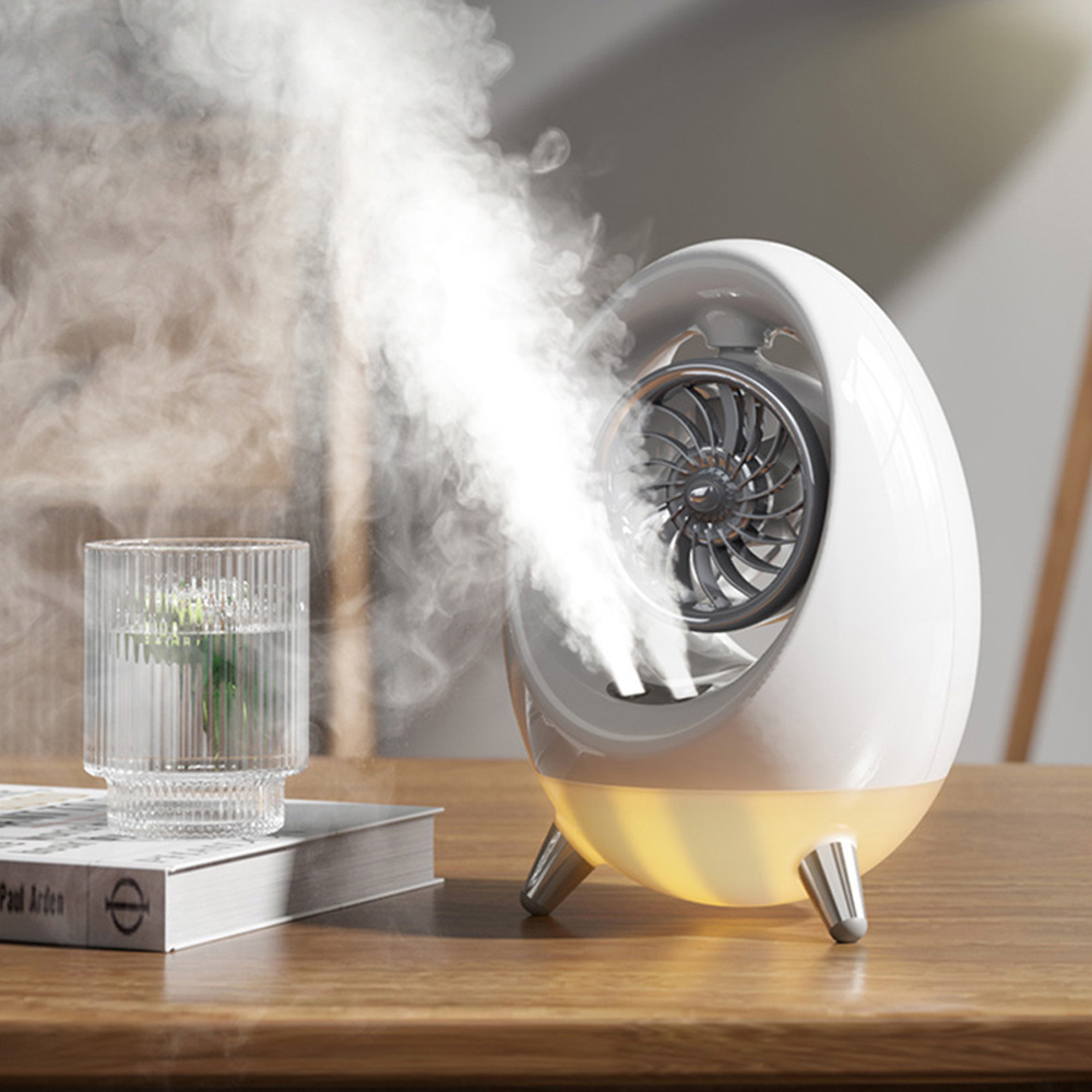 Ein weißer Luftbefeuchter mit Ventilator stößt Nebel neben einem Glas Wasser auf einem Holztisch aus.