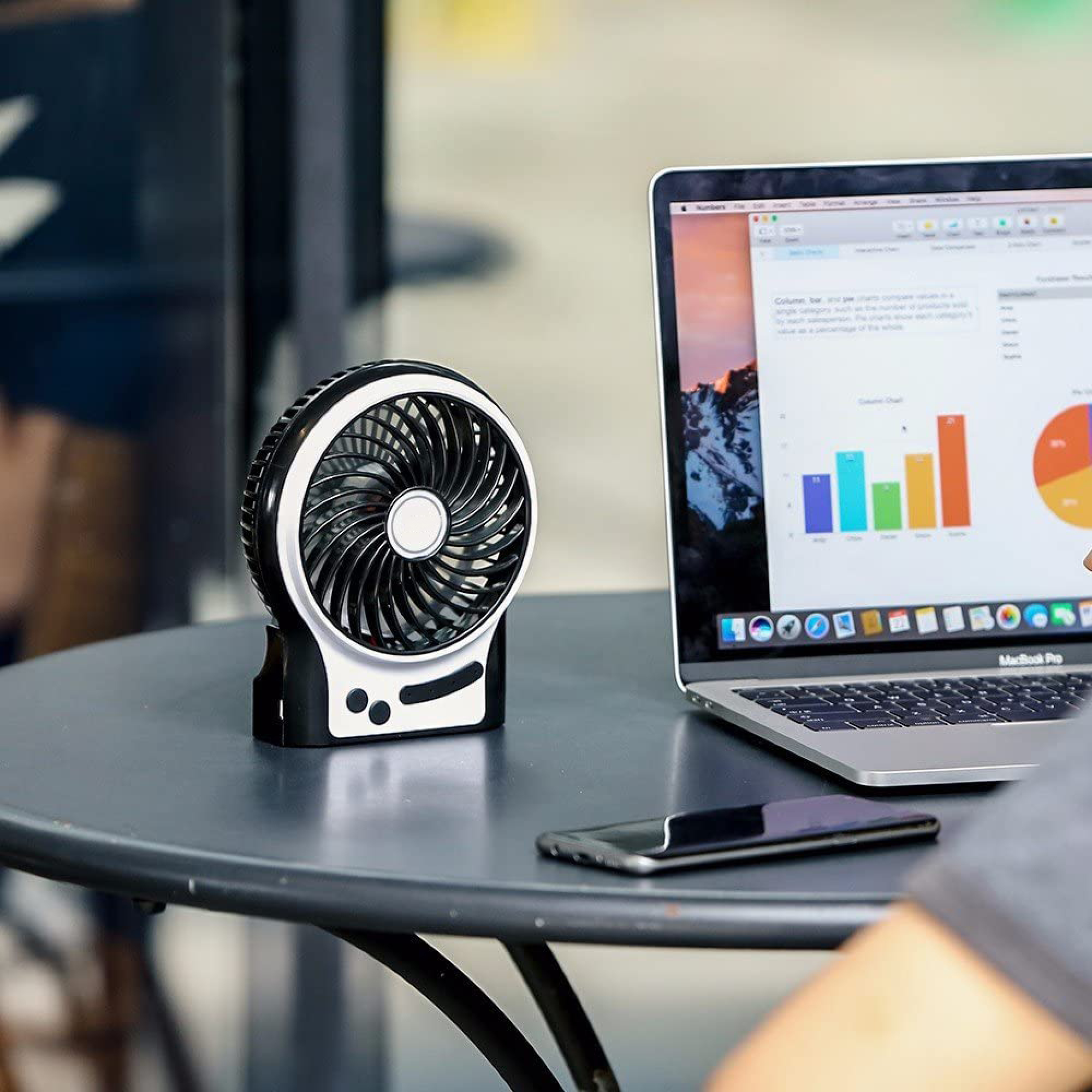 Ein kleiner schwarzer Ventilator steht neben einem Laptop mit Diagrammen.