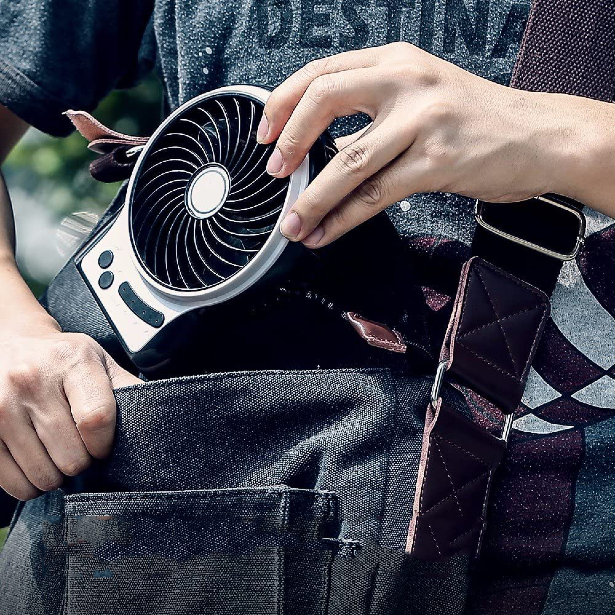 Person hält einen kleinen Ventilator in der Hand, der an einer Tasche befestigt ist.