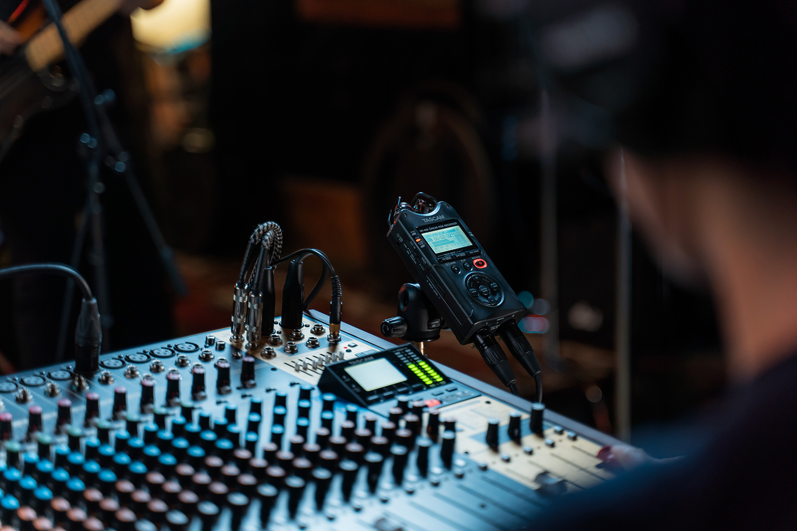 Mixer audio con registratore, cavi e spalla di persona in primo piano.