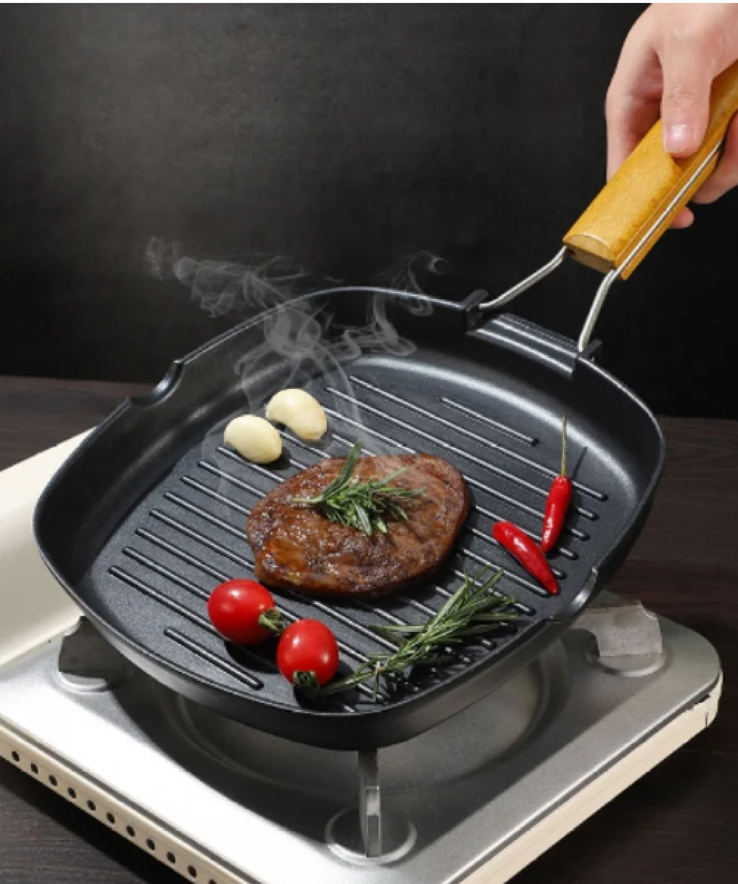 Ein Steak wird in einer Grillpfanne mit Kirschtomaten, Knoblauch und Chilis gebraten.
