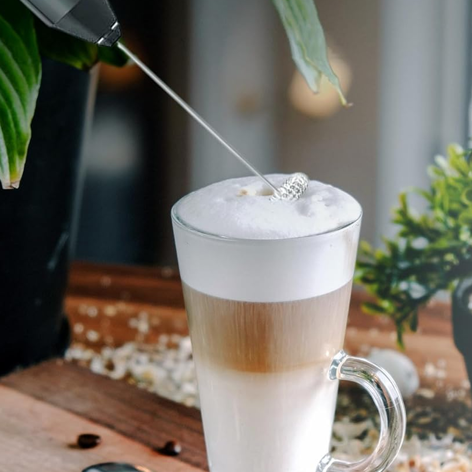 Ein Milchaufschäumer rührt in einem Glas Latte Macchiato mit viel Schaum.