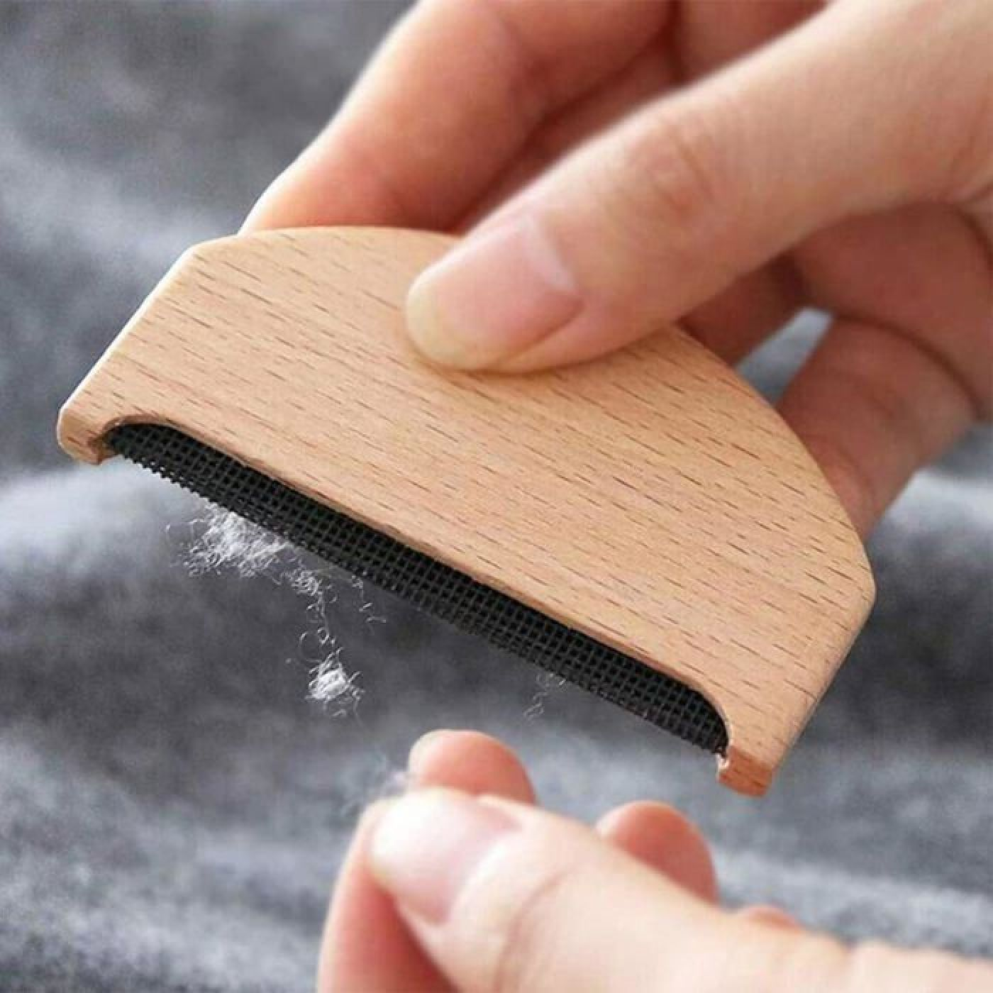 Holzkleiderbürste entfernt Flusen von grauem Stoff, gehalten von Händen.