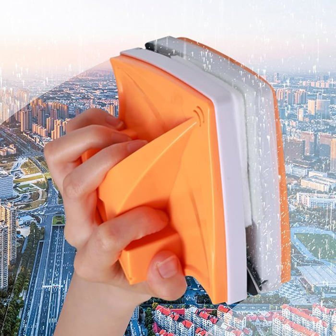 Hand hält einen orangefarbenen Fensterreiniger mit Magneten vor einer Stadtkulisse.