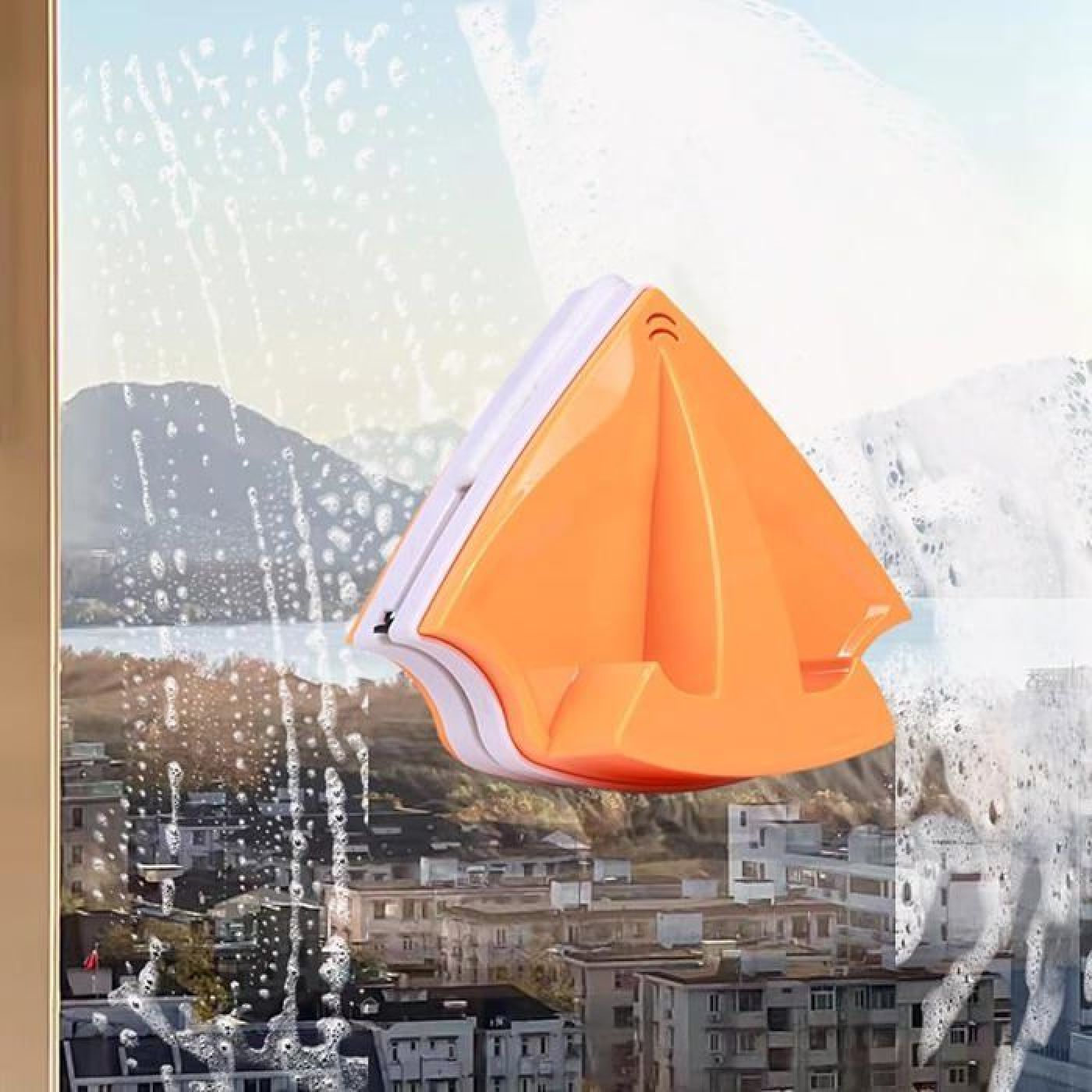 Ein orangefarbener Fensterreiniger mit Magneten auf einem schaumigen Fenster.